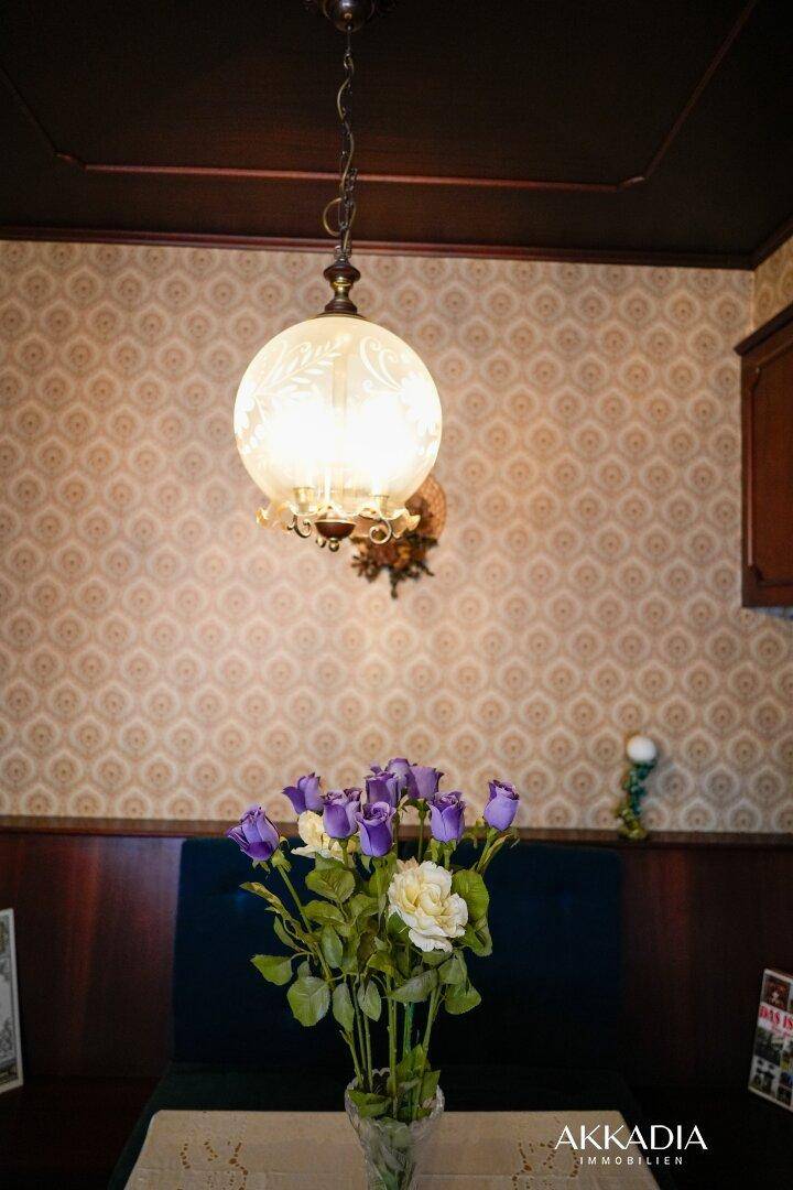 Dekorative Blumen und eine klassische Hängelampe im Essbereich mit gemusterter Tapete.