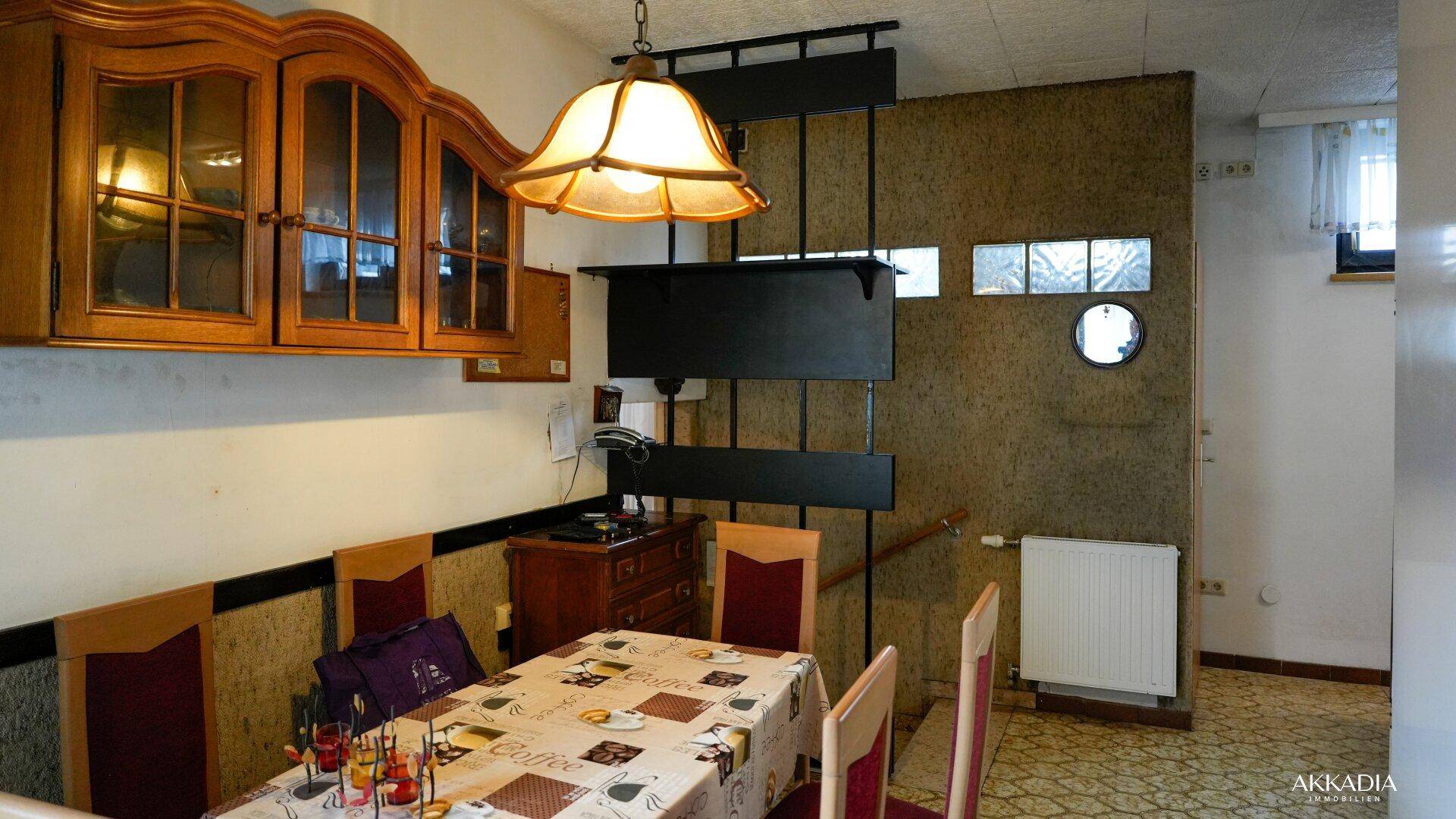 Essbereich mit Holztisch, Stühlen und Zugang zu einer Treppe.