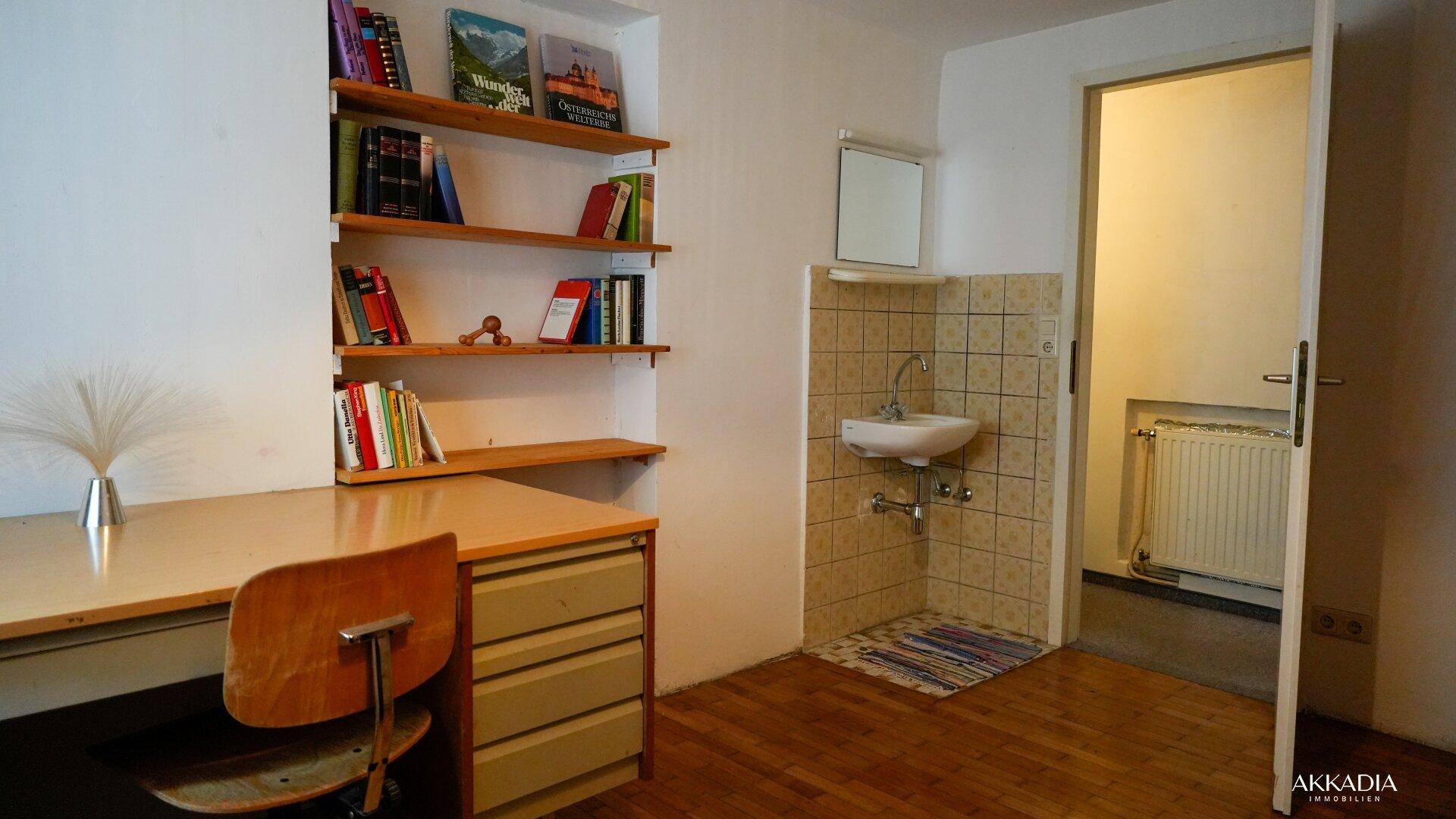 Arbeitszimmer mit Bücherregal, Schreibtisch und kleinem Waschbecken.