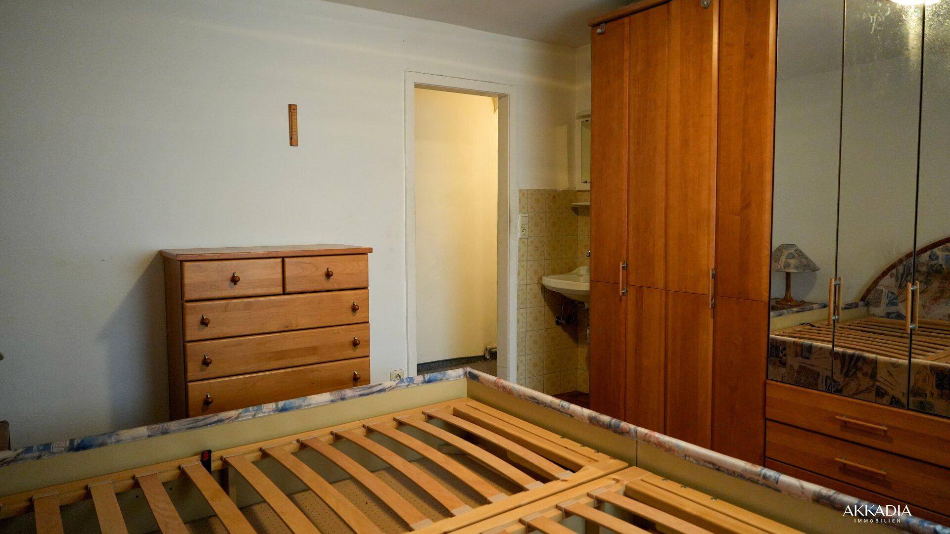 Schlafzimmer mit Kommode und Kleiderschrank, angrenzend an einen kleinen Waschbereich.