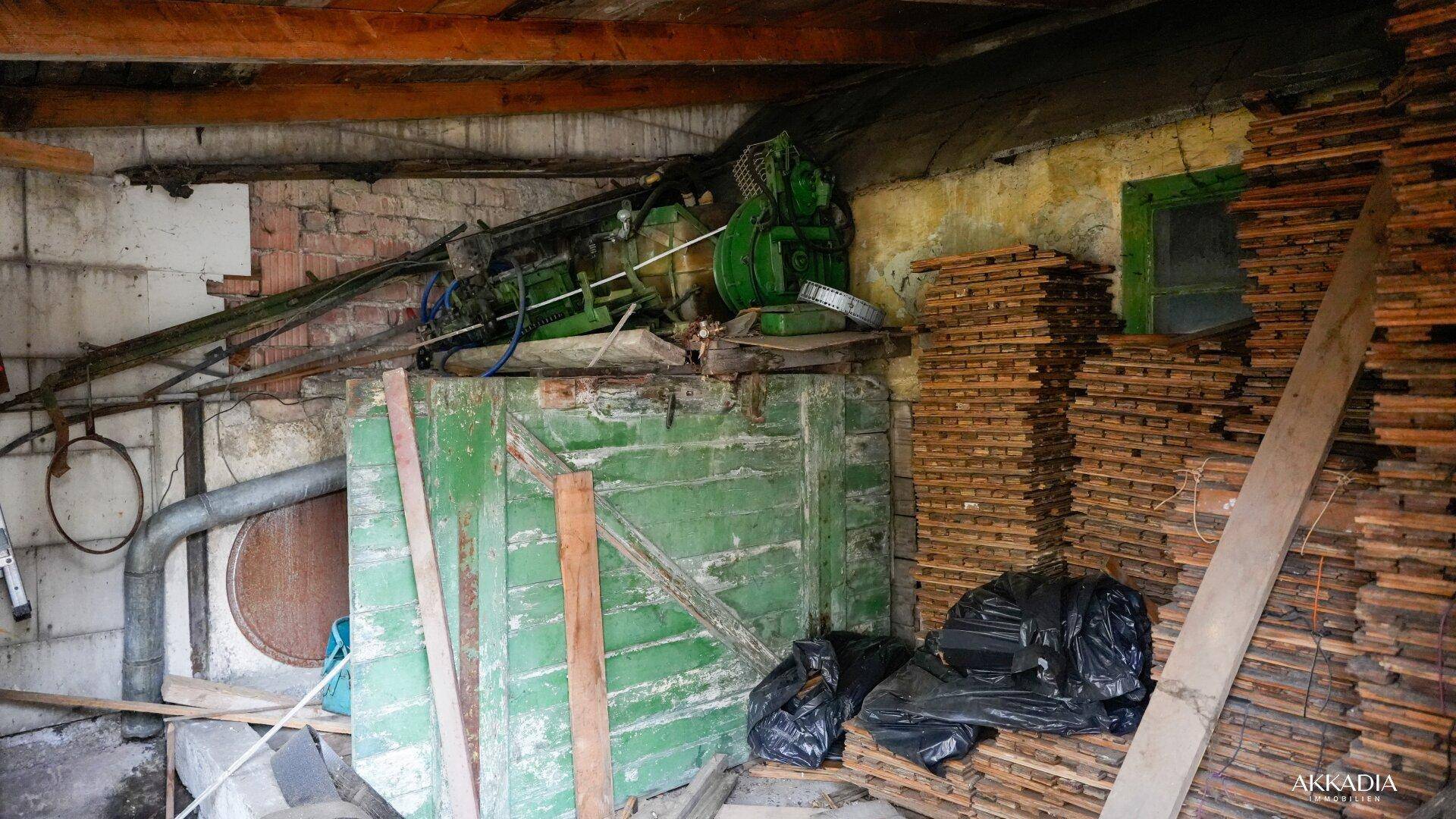 Kellerraum mit alter Maschine und Holzstapeln, geeignet als Lager oder Werkstatt.