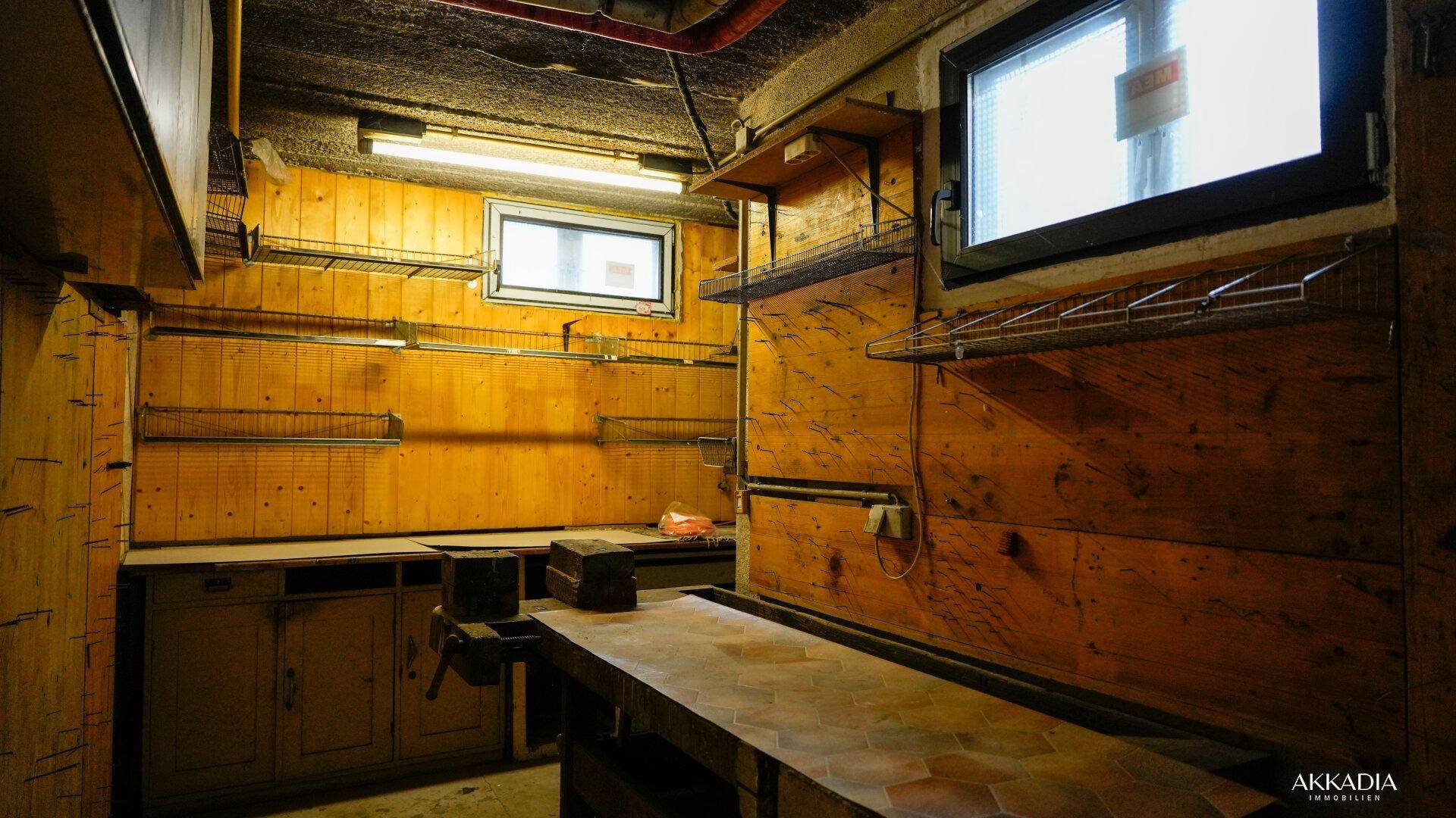 Werkstatt im Keller mit Arbeitsplatte, Regalen und Holzvertäfelung.