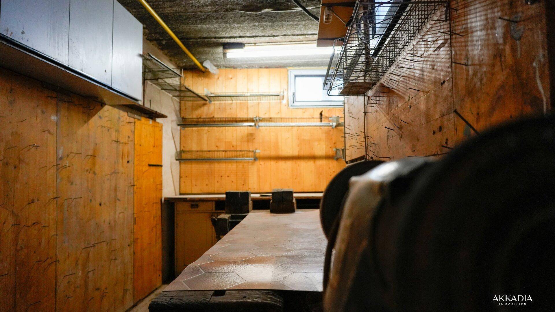 Kellerwerkstatt mit Arbeitsflächen, Regalen und Blick auf die Holzvertäfelung.