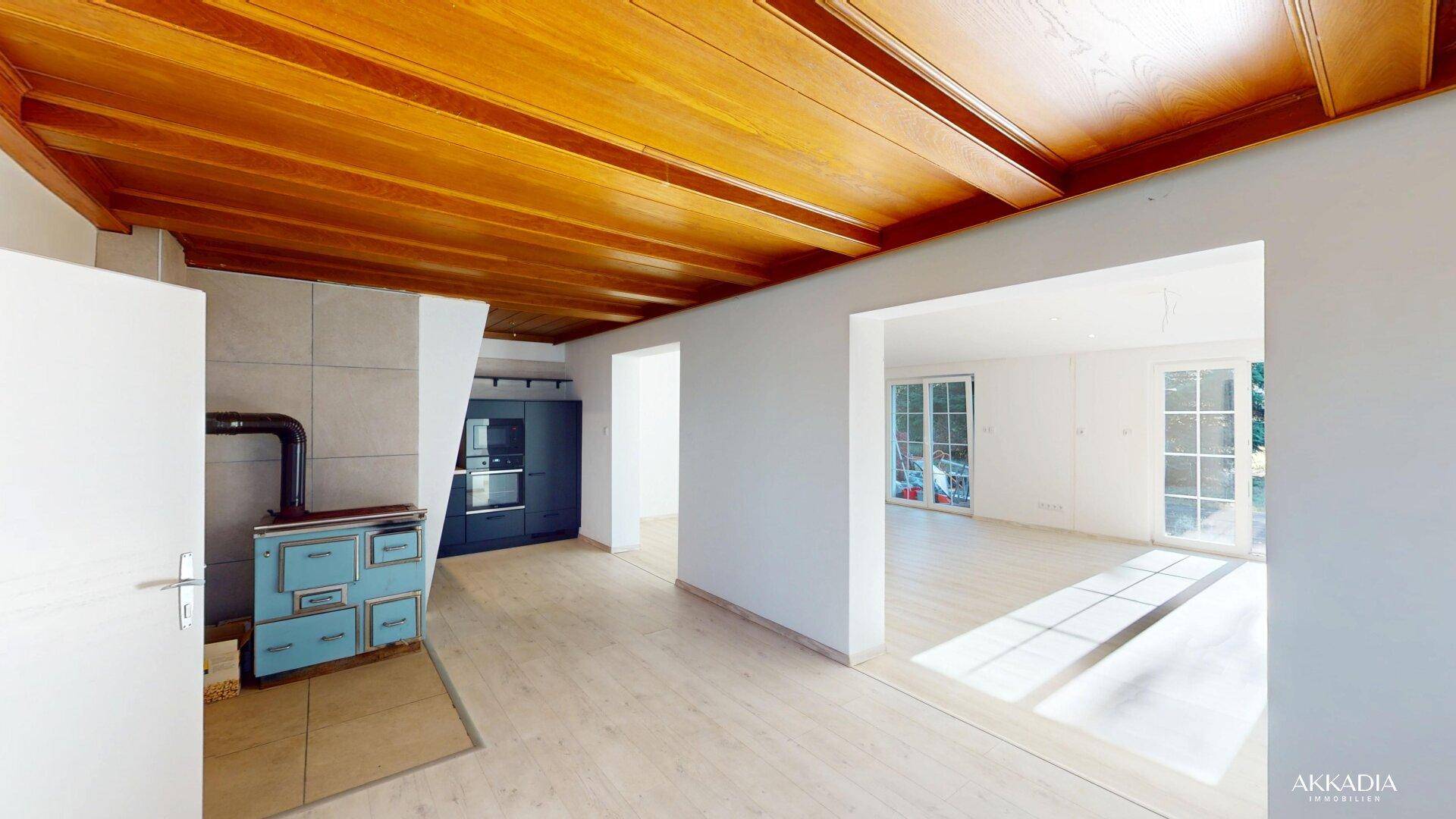 Offener Küchenbereich mit Holzbalkendecke, Kachelofen und Blick in den Wohnraum.