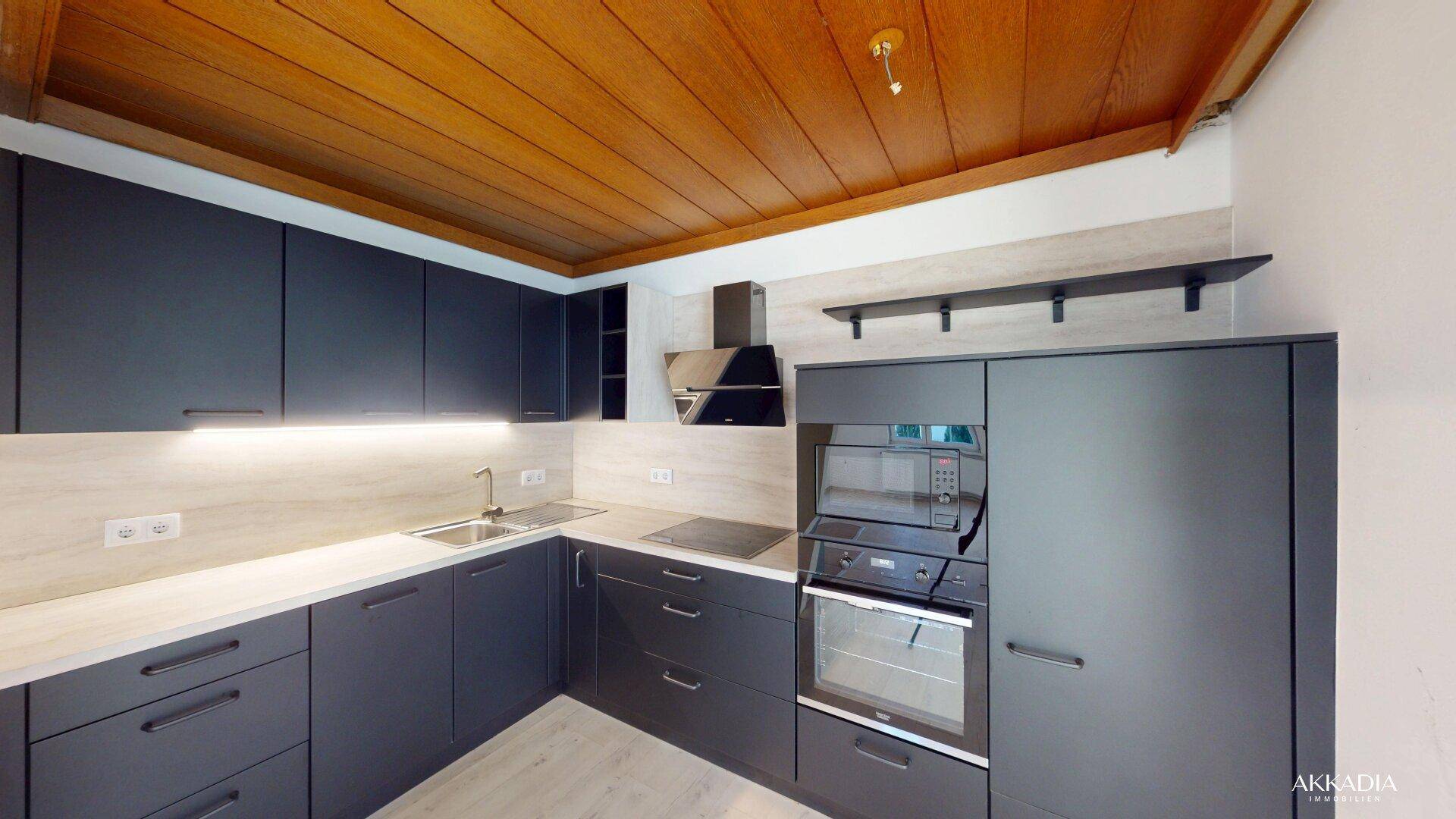 Moderne Einbauküche mit dunklen Schränken, integrierten Geräten und Holzbalkendecke.