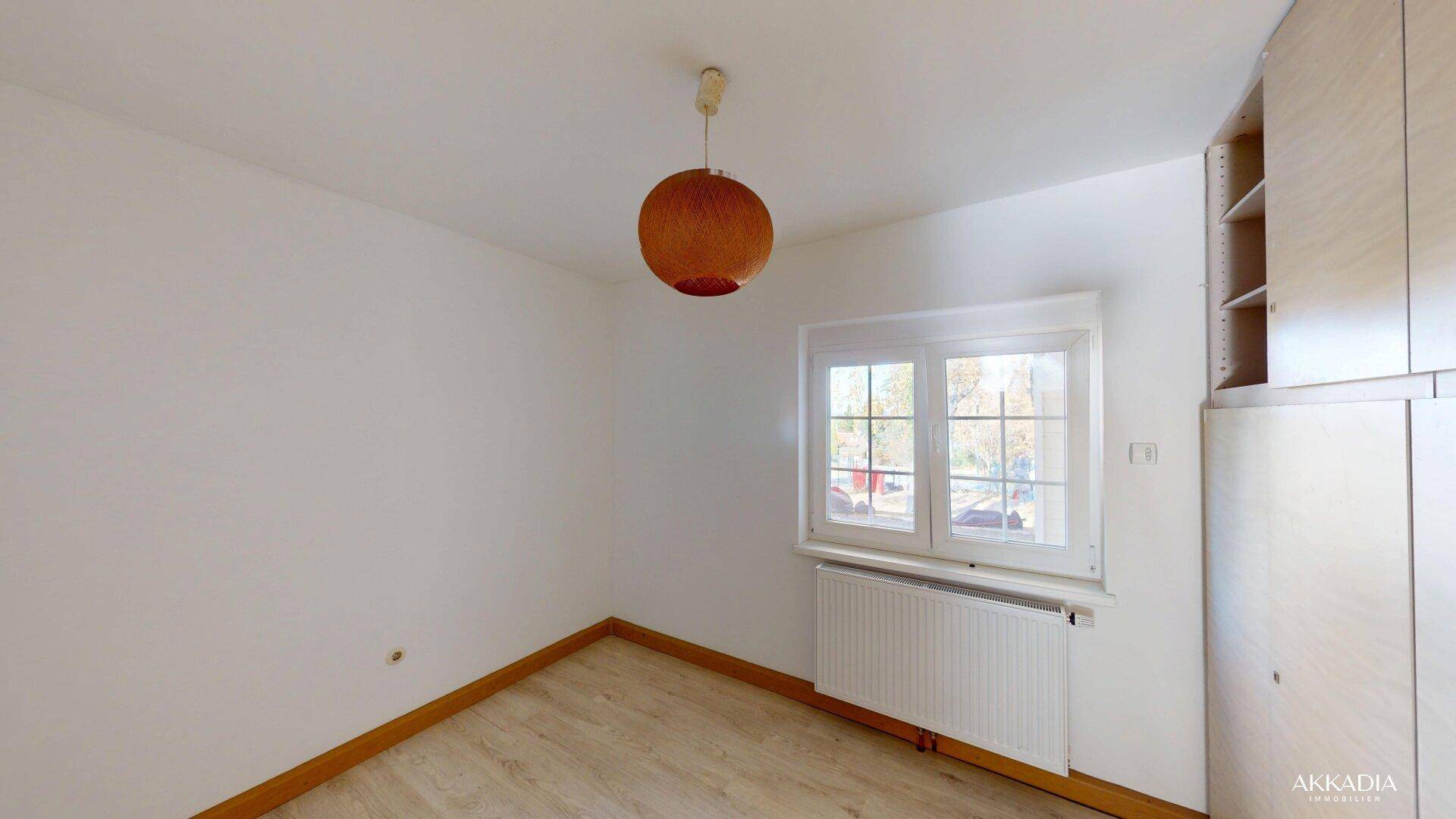 Helles Schlafzimmer mit Laminatboden, Fenster und einem praktischen Einbauschrank.