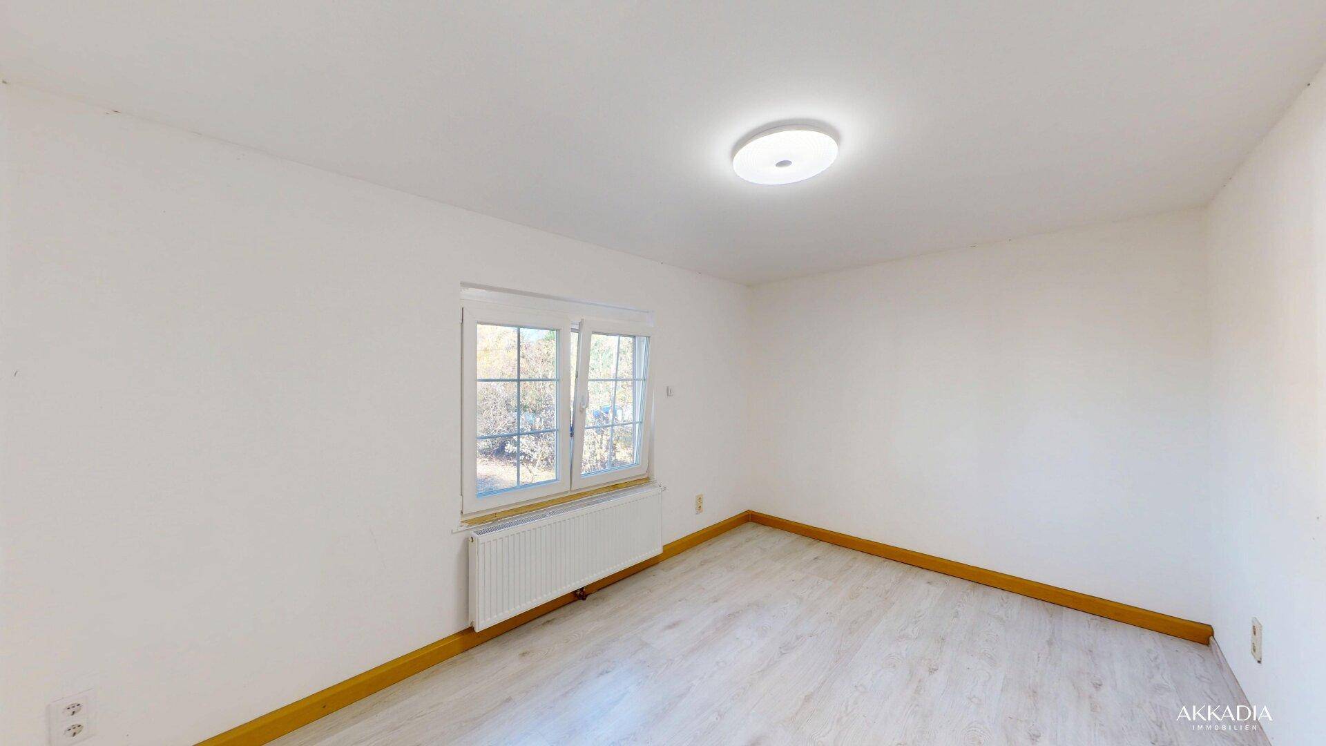 Helles Schlafzimmer mit Laminatboden, Fenster und weiß gestrichenen Wänden.