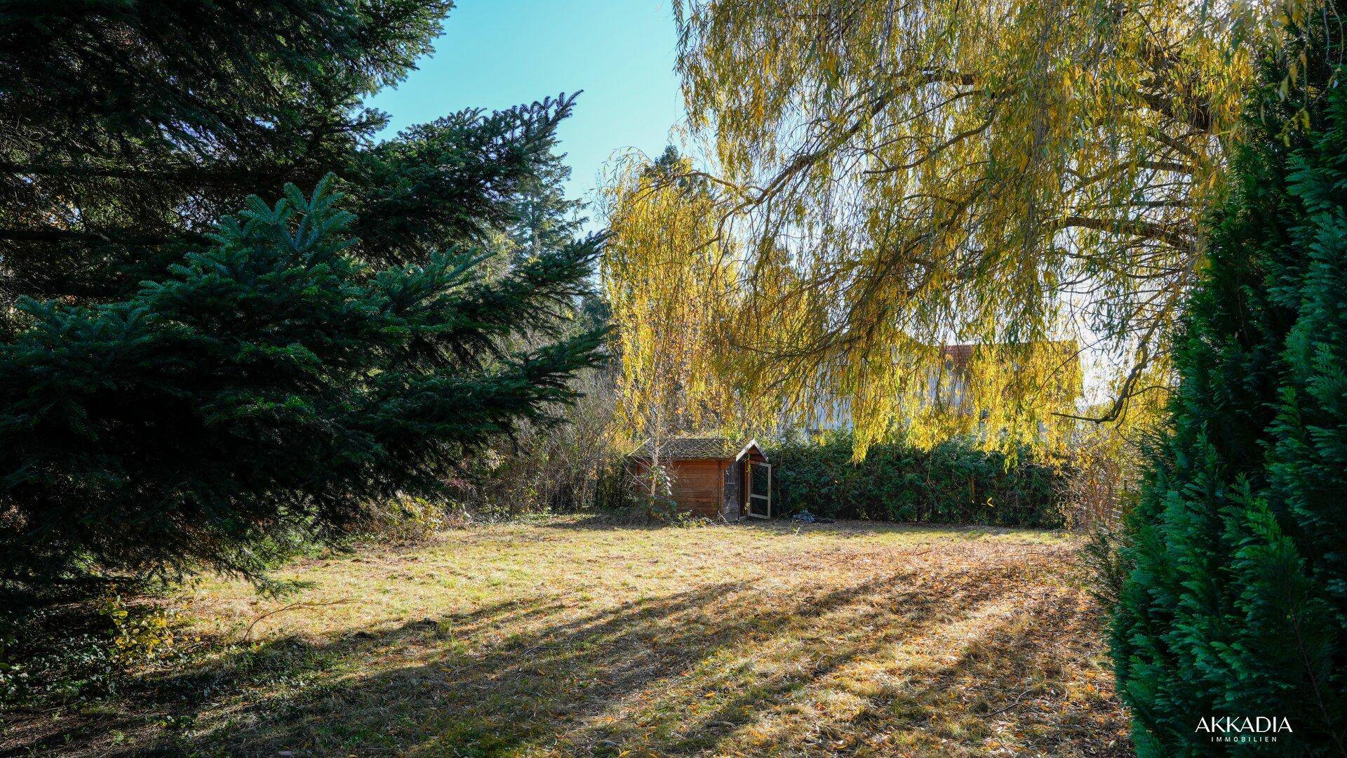 Großer Garten mit Rasenfläche, Bäumen und einem kleinen Gartenhaus im Hintergrund.