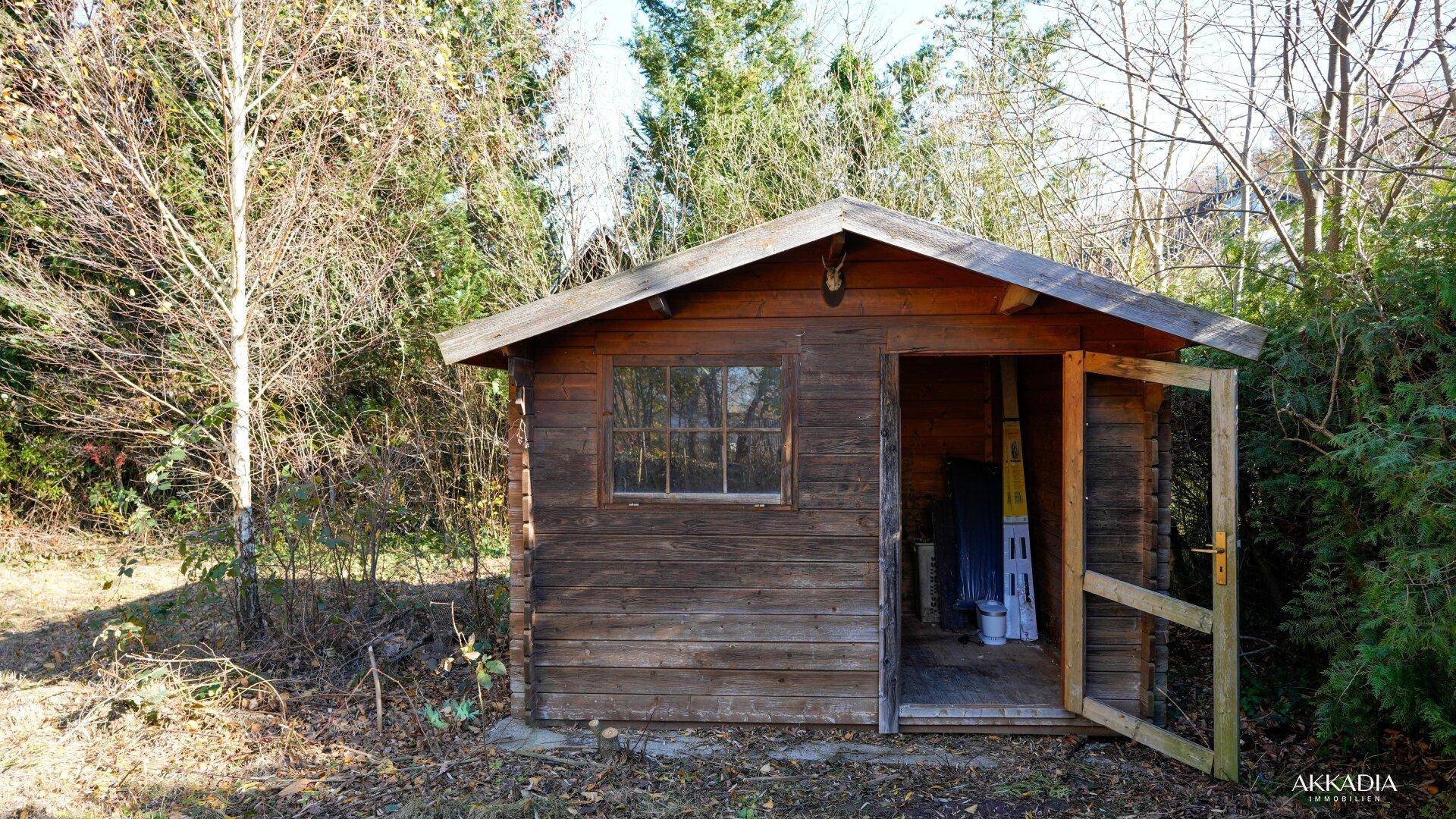 Kleines Gartenhaus aus Holz mit Fenster und offener Tür im grünen Garten.