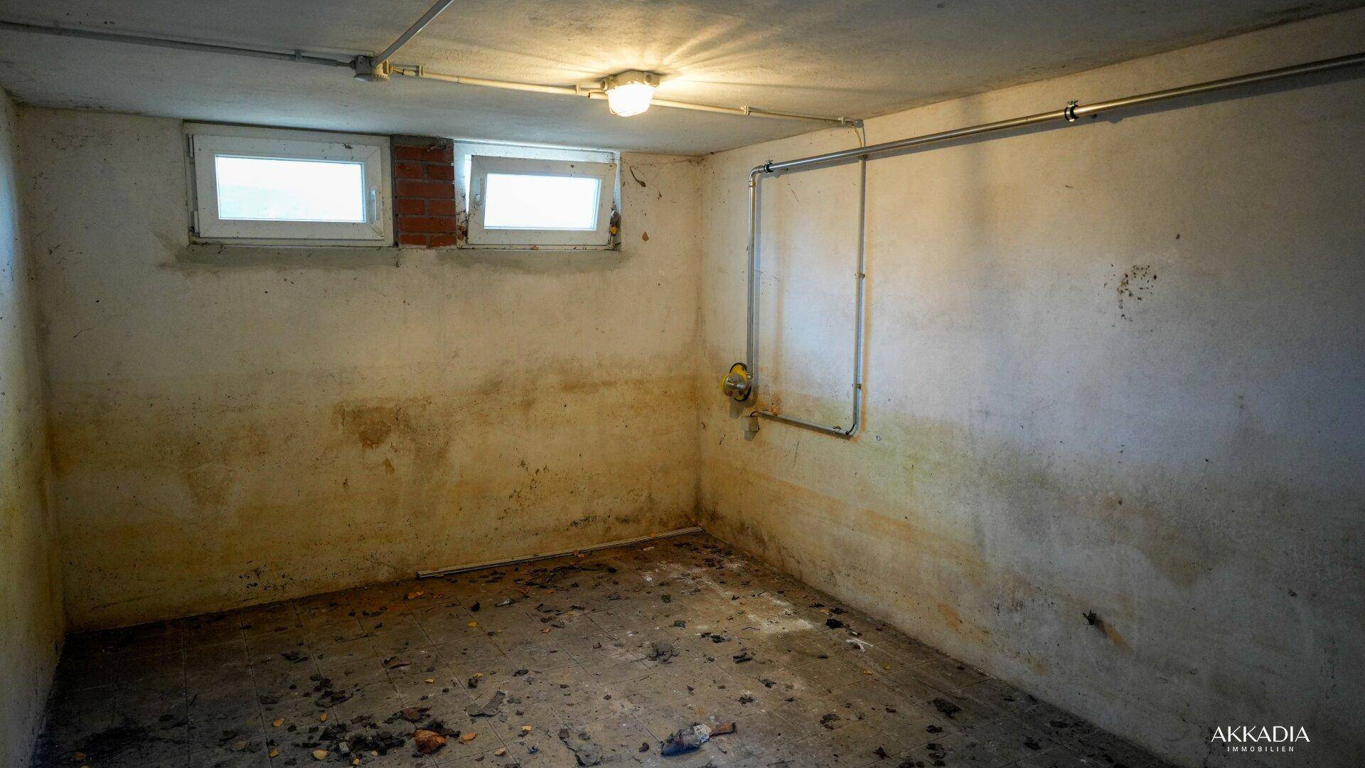 Unfertiger Kellerraum mit kleinen Fenstern und sichtbaren Rohren, renovierungsbedürftig.