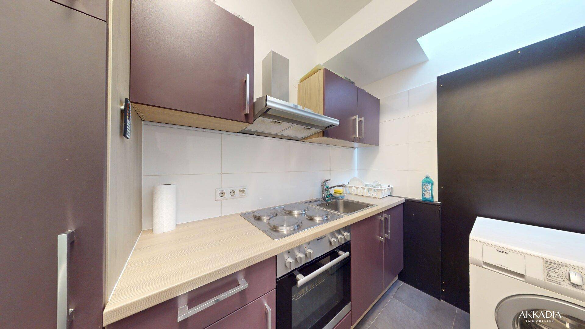 Funktionale Küche mit dunklen Schränken, Elektroherd und Dachfenster für natürliches Licht.