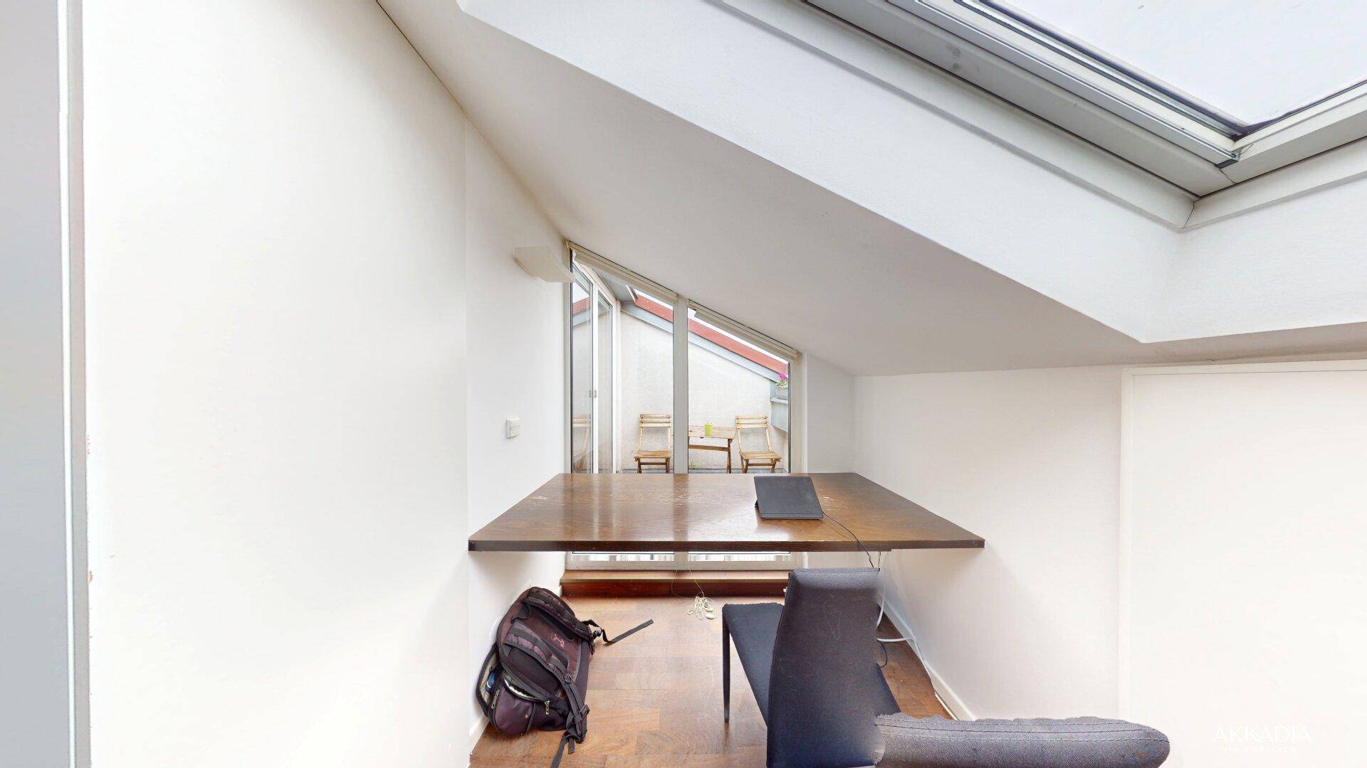 Heller Arbeitsbereich mit großem Schreibtisch und Zugang zu einem kleinen Balkon.