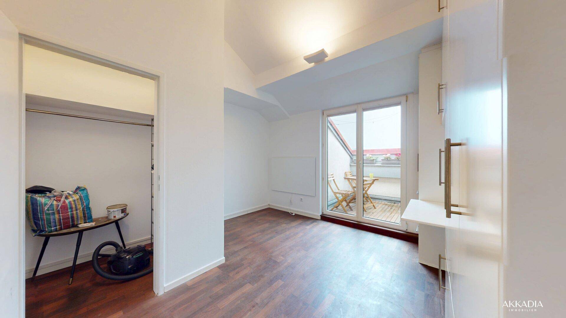 Helles Zimmer mit Holzboden, Zugang zum Balkon und integriertem Stauraum.