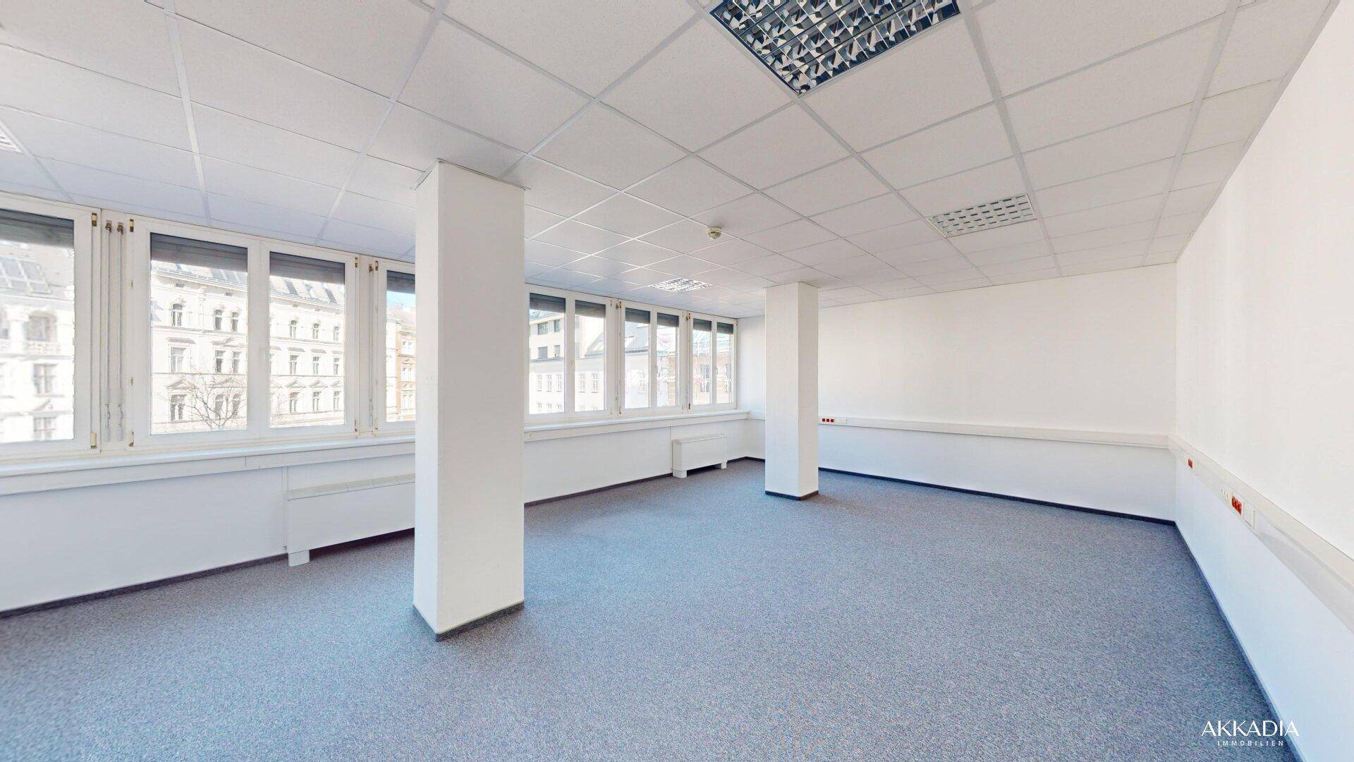Geräumiger Büroraum mit Säulen, Teppichboden und einer langen Fensterfront für natürliches Licht.