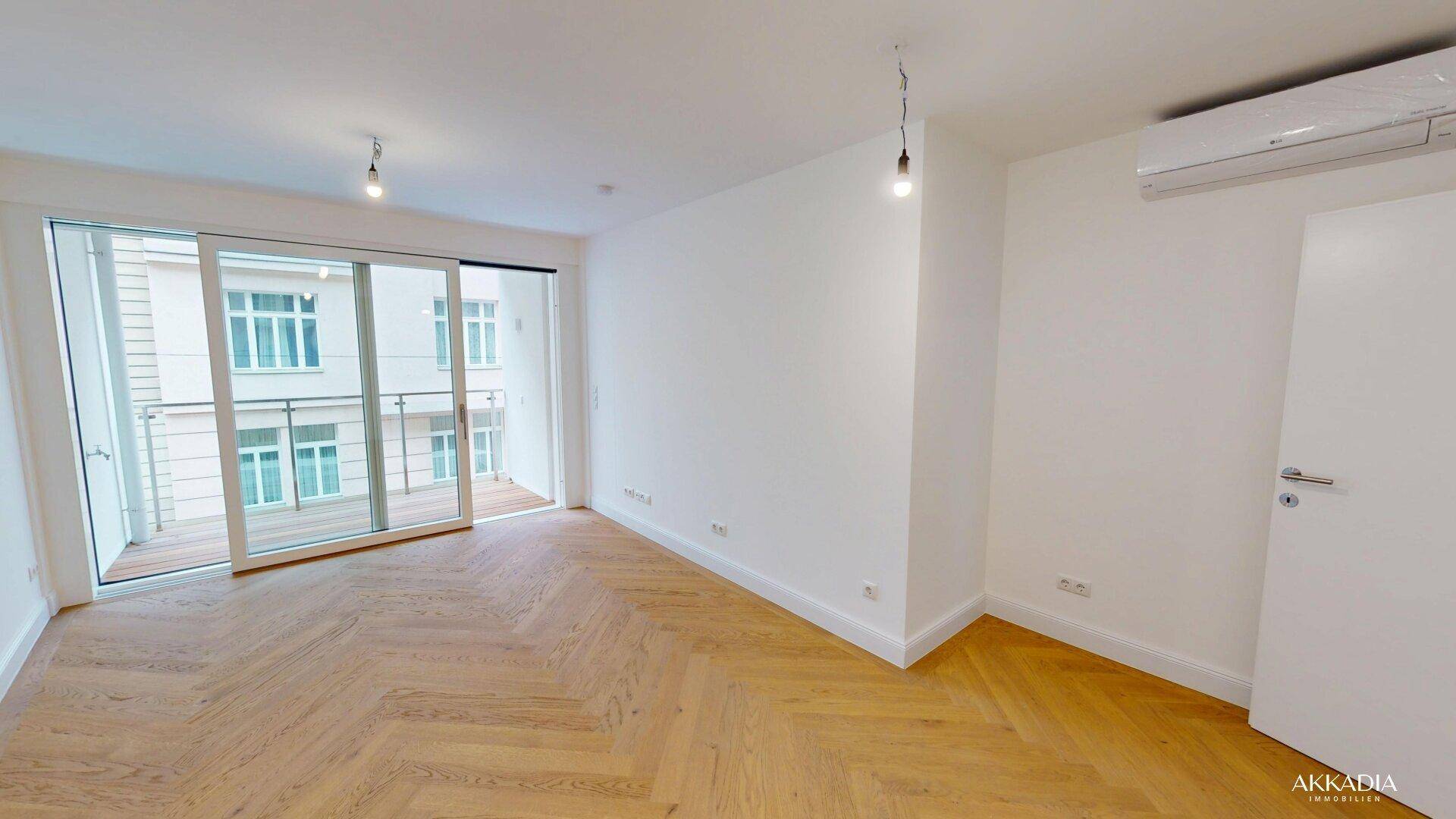 Heller Wohnraum mit elegantem Fischgrätparkett, großen Schiebetüren zum Balkon und Klimaanlage.