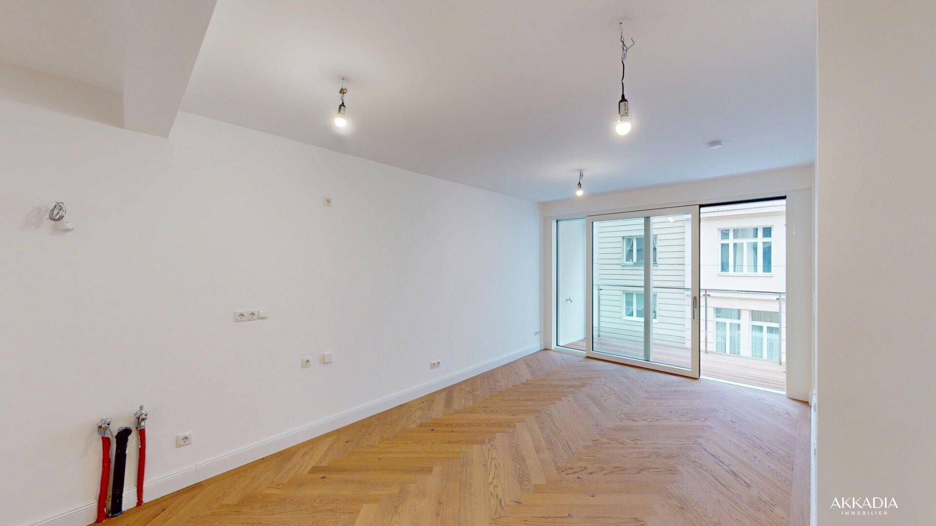 Heller Wohnraum mit Fischgrätparkett und großen Schiebetüren, die zum Balkon führen.