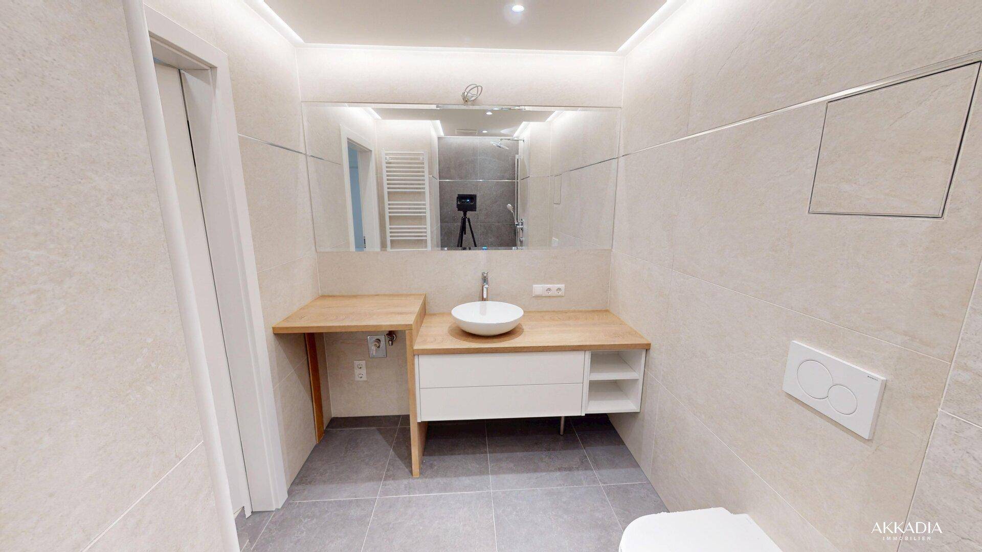 Modernes Badezimmer mit Einzelwaschbecken, Holzplatte, großem Spiegel und Wand-WC.