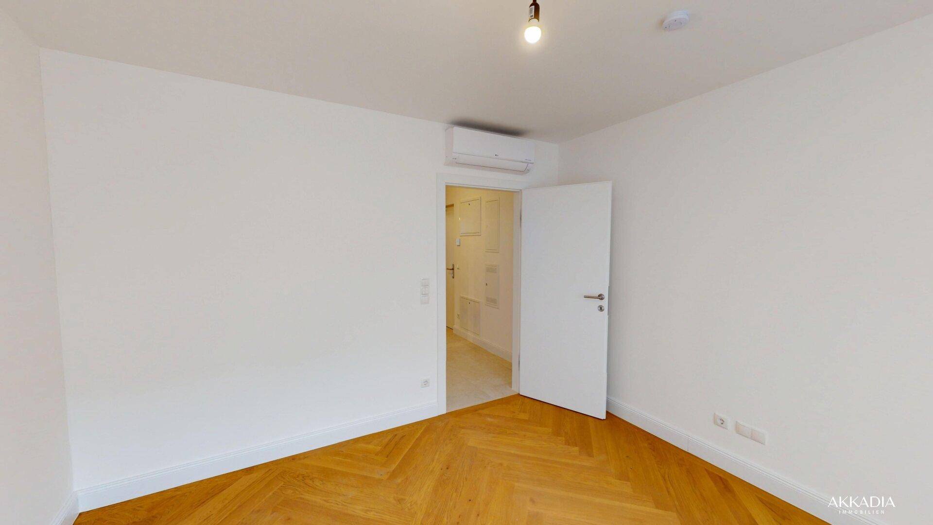 Heller Raum mit Fischgrätparkett, Klimaanlage und Zugang zu einem weiteren Zimmer.