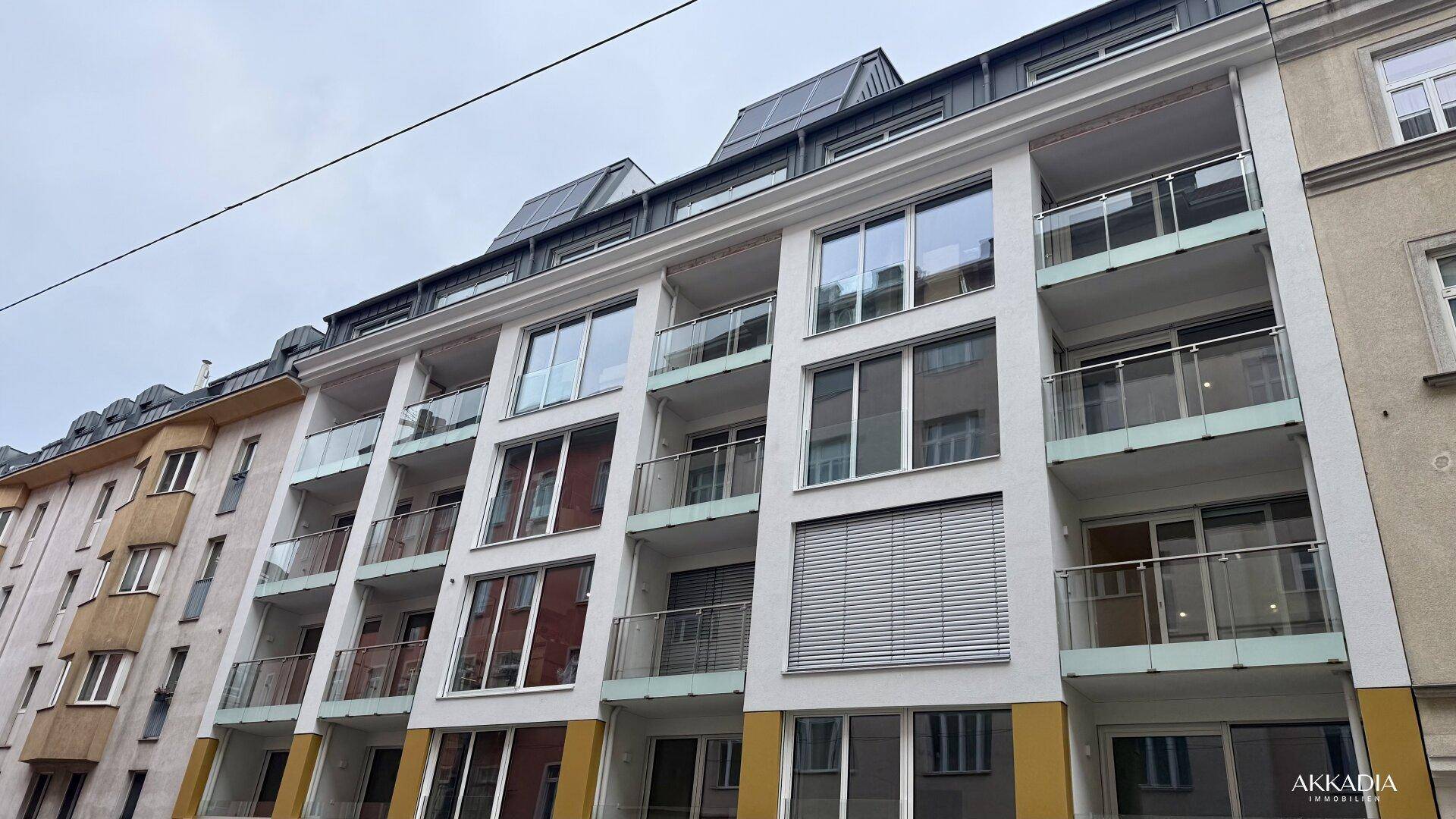 Moderne Wohnhausfassade mit vielen Balkonen, großen Fenstern und Photovoltaikanlage auf dem Dach.