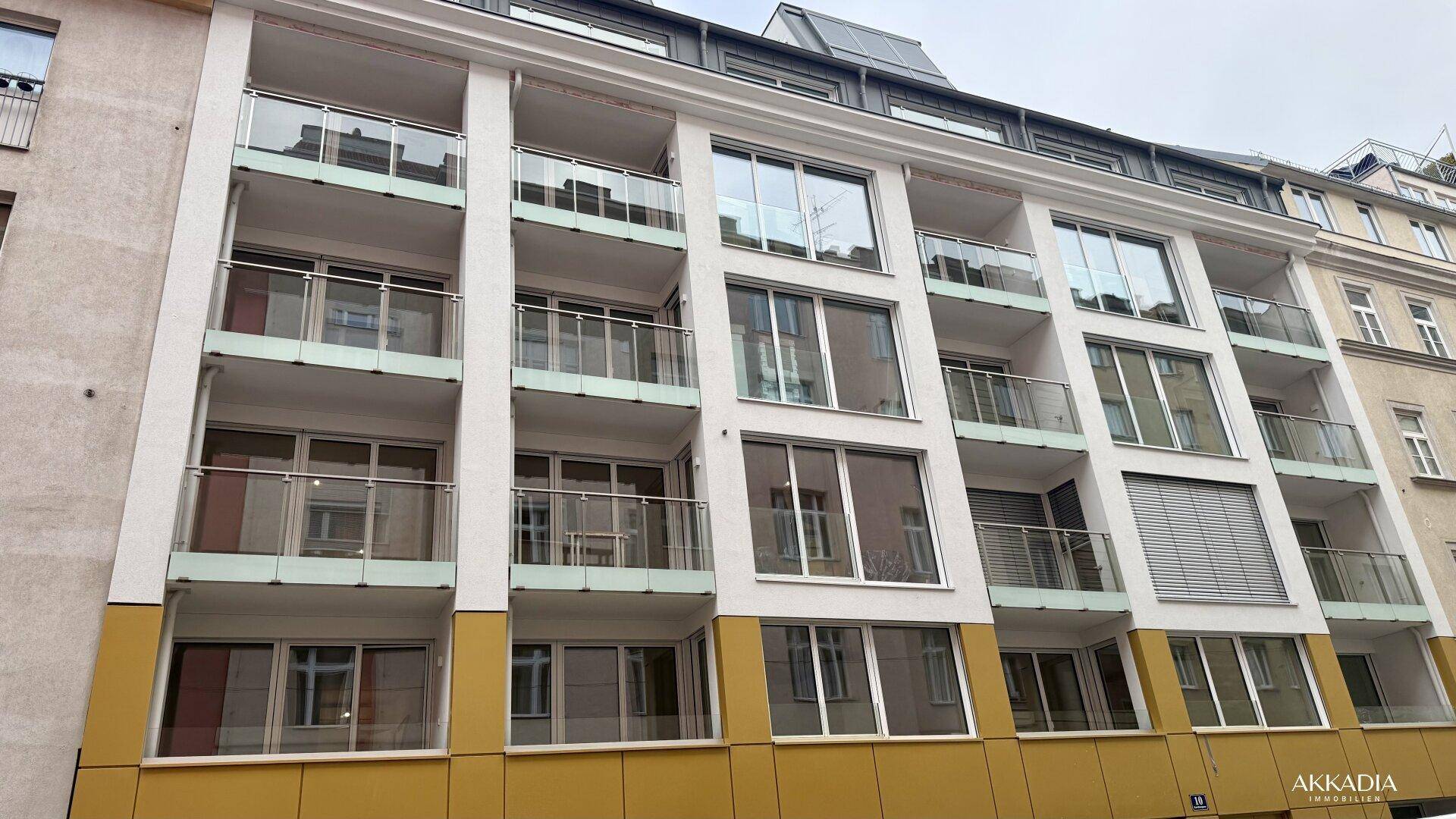 Moderne Wohnhausfassade mit vielen Balkonen, großen Fenstern und Photovoltaikanlage auf dem Dach.