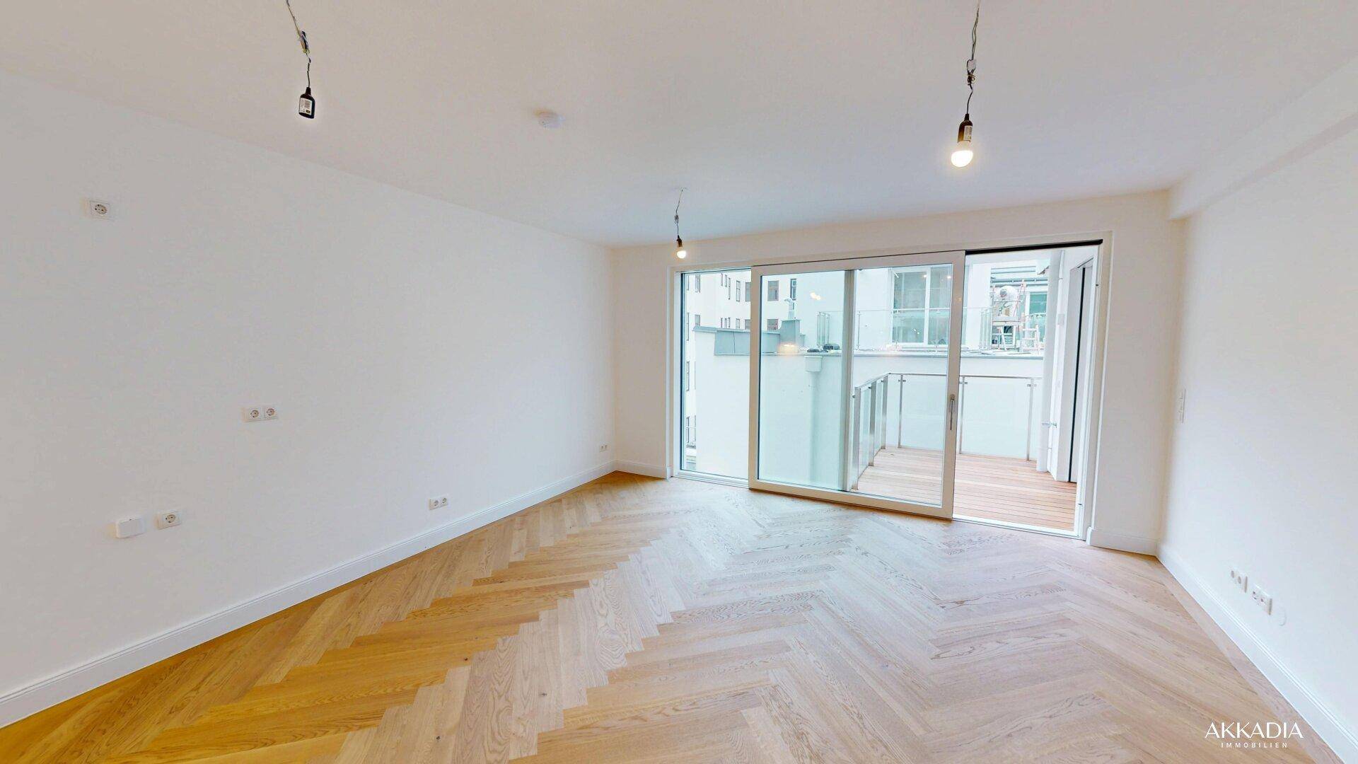Heller, unmöblierter Raum mit elegantem Fischgrätparkett und Schiebetüren zum Balkon.
