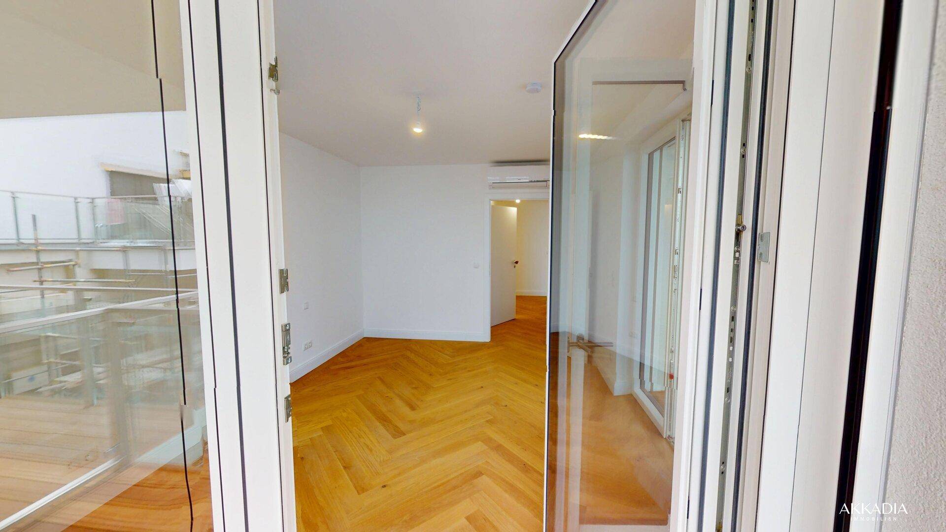 Helles Zimmer mit Fischgrätparkett und Zugang zu einem sonnigen Balkon mit Stadtblick.