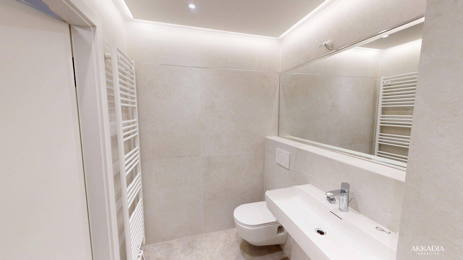 Modernes Gäste-WC mit Wand-WC, Waschtisch und beheiztem Handtuchhalter.