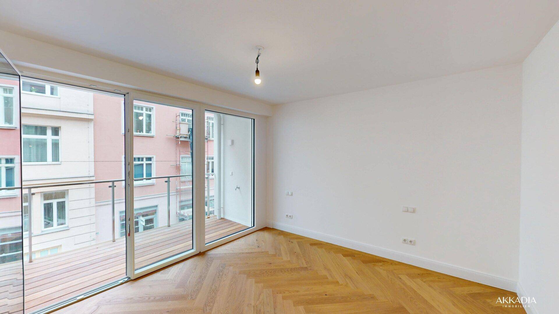 Lichtdurchflutetes Zimmer mit Fischgrätparkett und großem Balkonzugang mit Stadtblick.