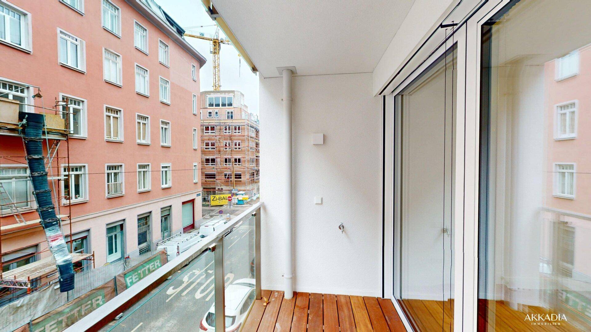 Moderner Balkon mit Holzfußboden und Glasgeländer, bietet einen weiten Blick auf die Stadt und umliegende Gebäude.