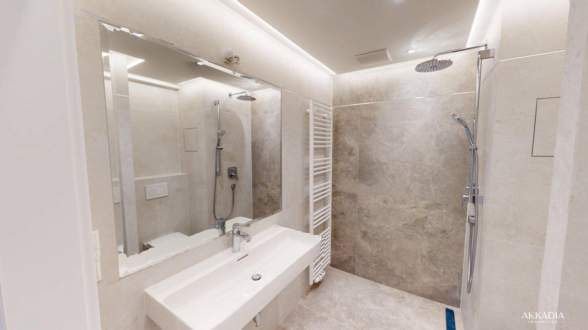Modernes Badezimmer mit Regendusche, Waschtisch und großem Spiegel über dem Waschtisch.