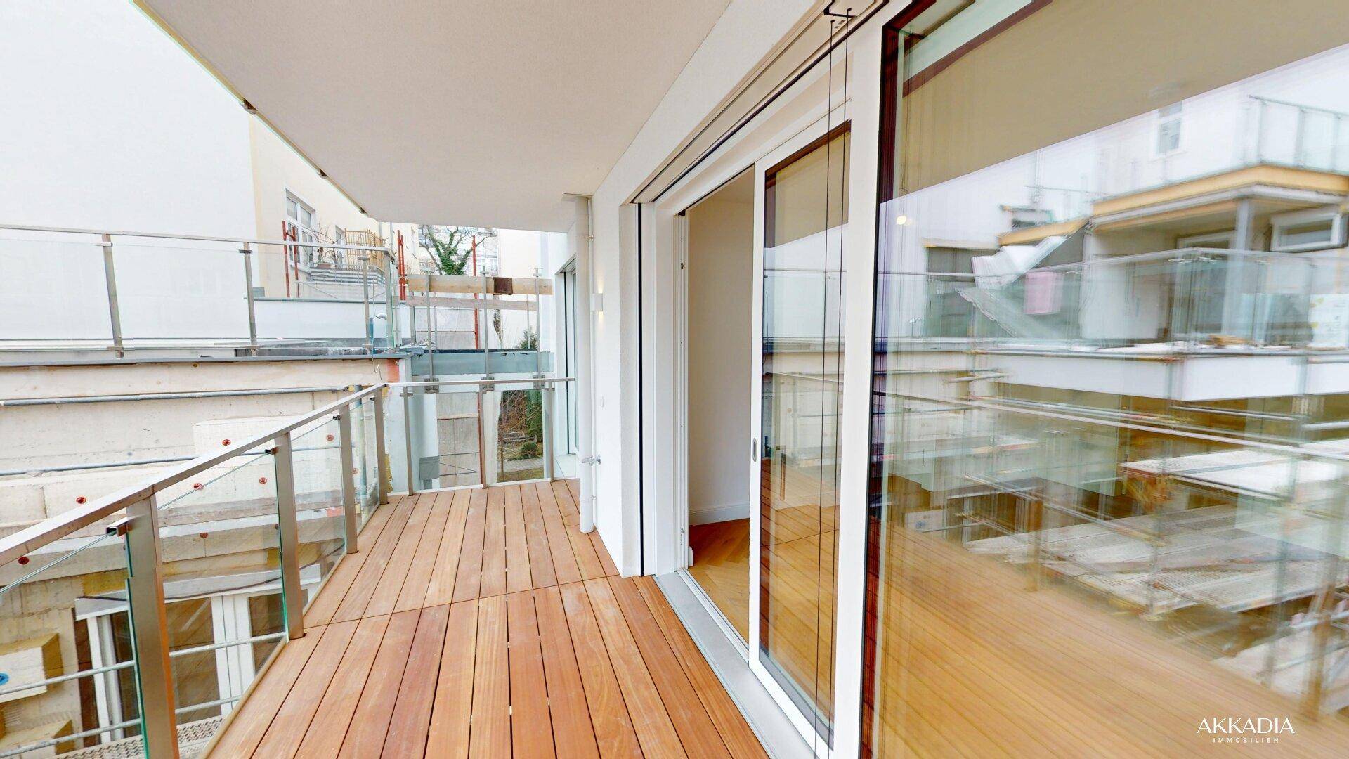 Geräumiger Balkon mit Holzbelag und Glasgeländer, ideal für entspannte Stunden im Freien.