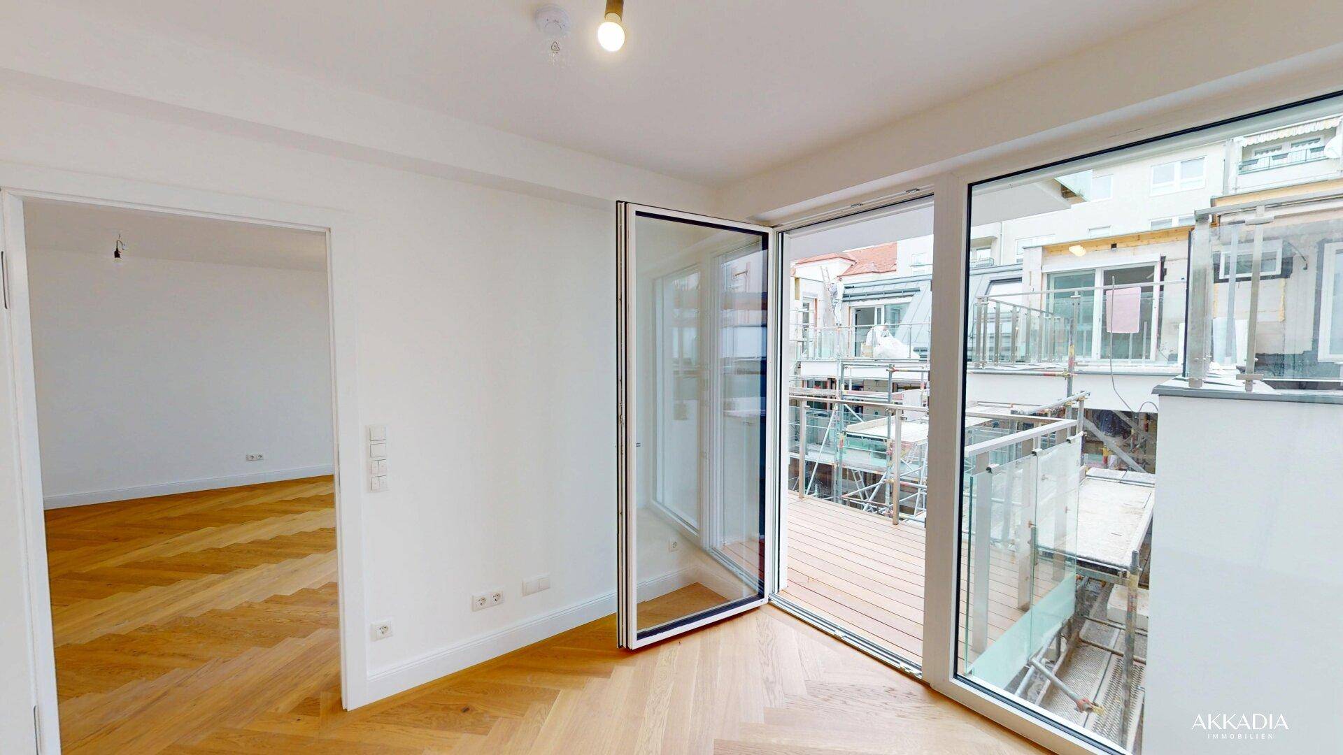 Heller Raum mit Fischgrätparkett und großen Falttüren, die zum Balkon führen.