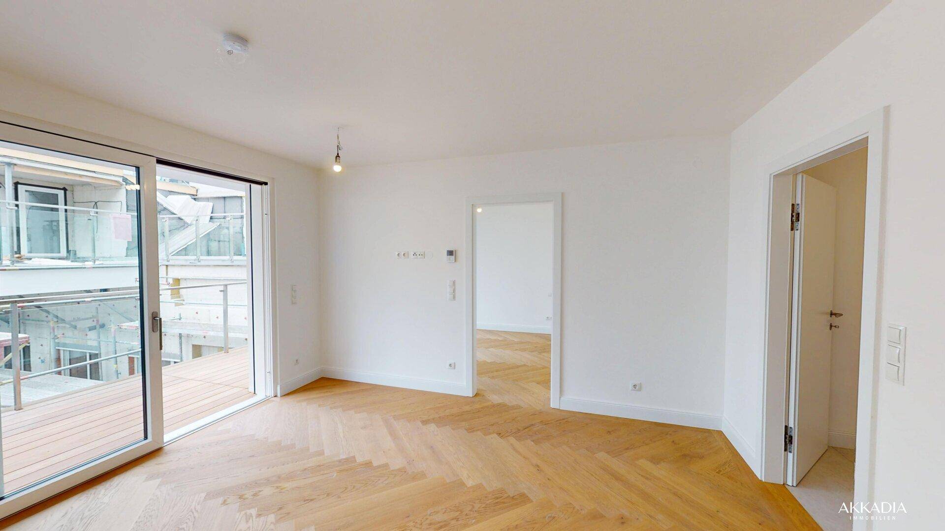 Heller Wohnraum mit elegantem Fischgrätparkett und direktem Zugang zum Balkon.