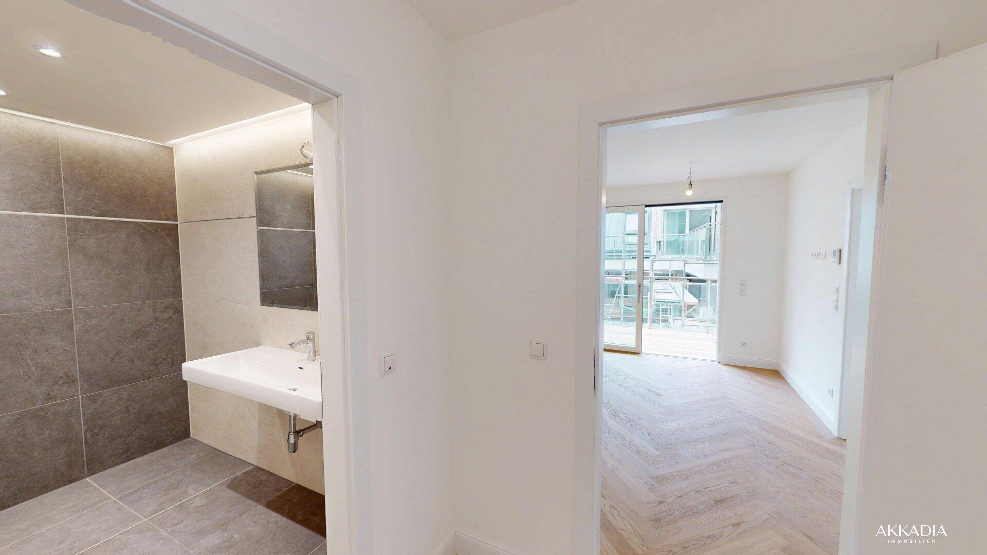 Flur mit Blick in ein modernes Badezimmer und einen hellen Wohnbereich mit Balkonzugang.