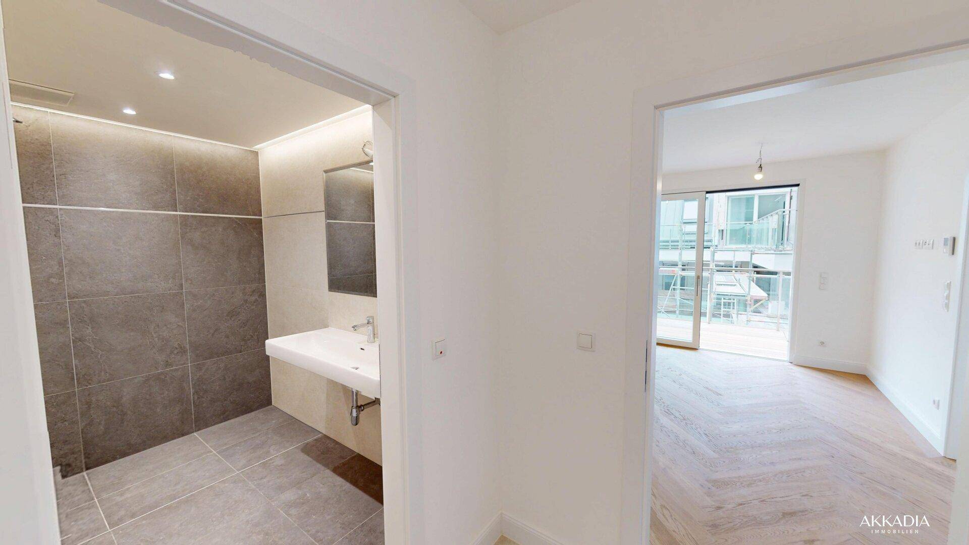 Flur mit Blick in ein modernes Badezimmer und einen hellen Wohnbereich mit Balkonzugang.