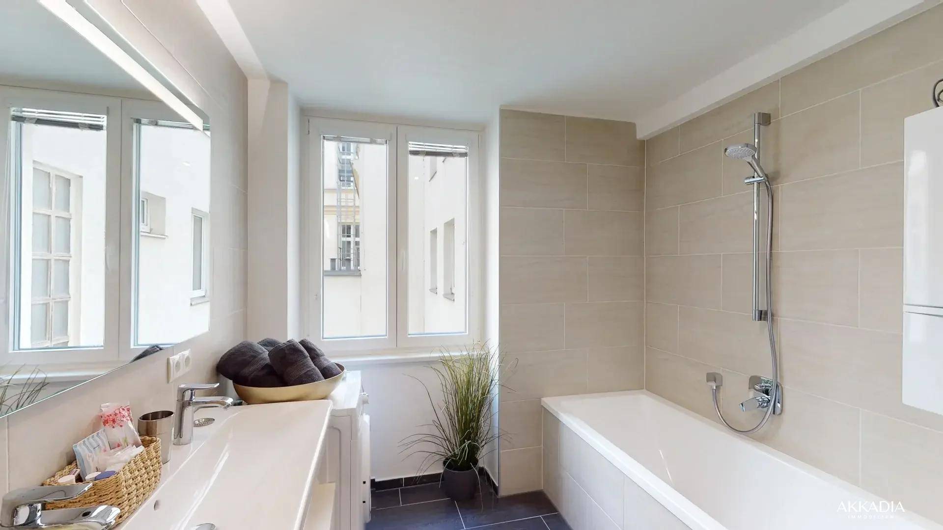 Helles Badezimmer mit Badewanne, Doppelwaschbecken und Fenster.