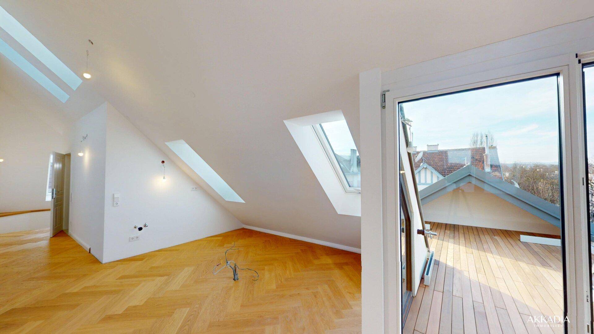 Heller Dachgeschossraum mit schrägen Wänden, Fischgrätparkett und Zugang zu einer Dachterrasse.