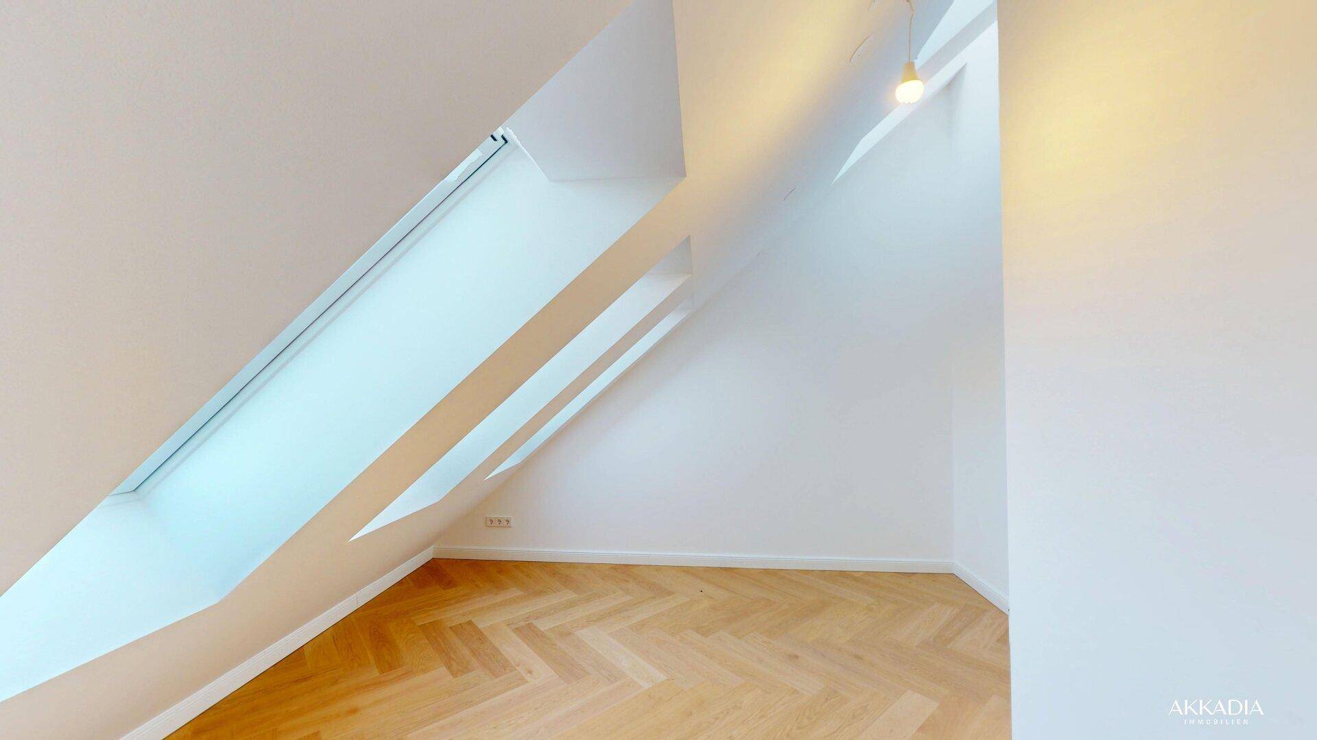 Heller Dachgeschossraum mit Fischgrätparkett und schrägen Dachfenstern für viel Tageslicht.