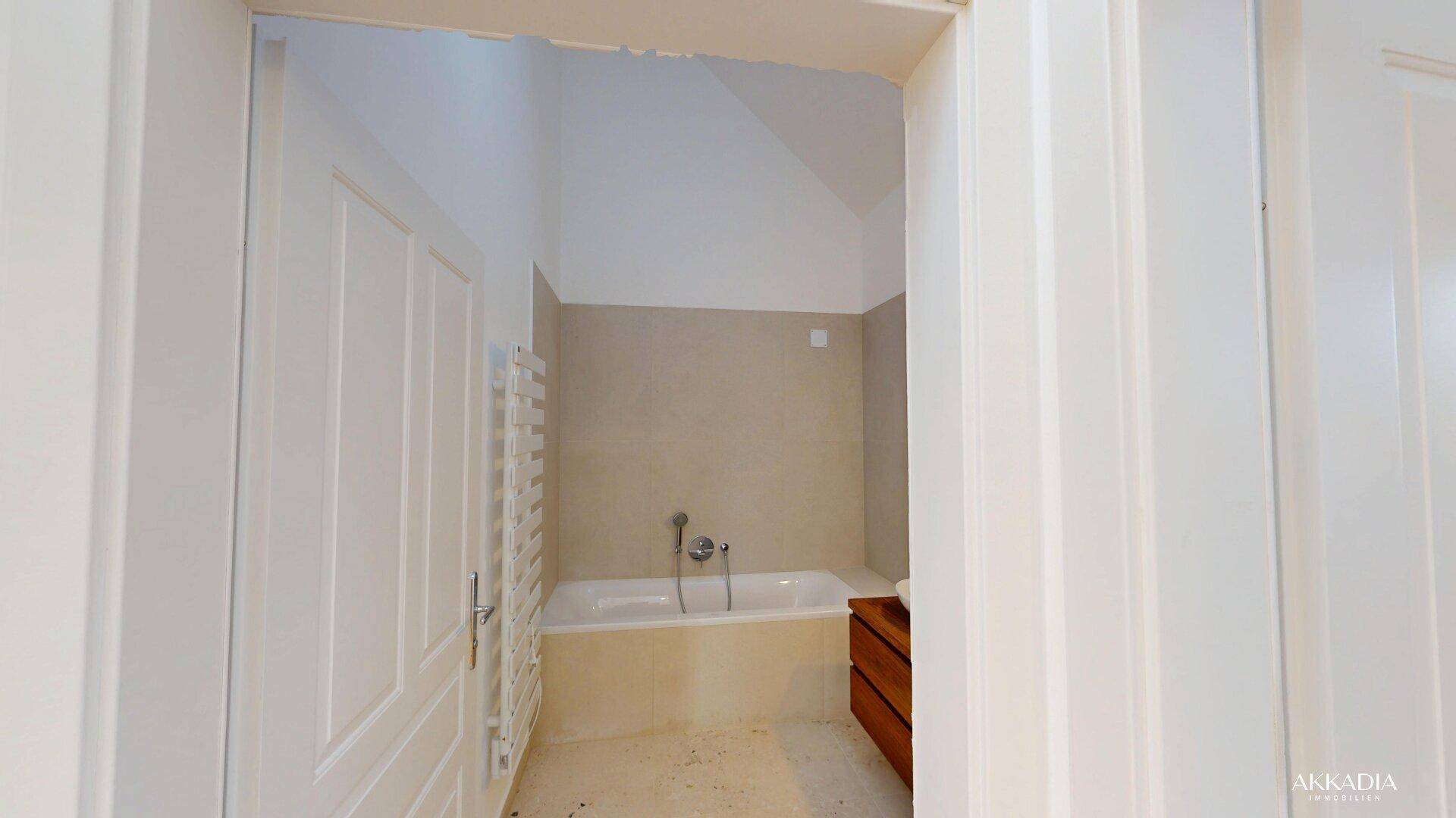 Modernes Badezimmer mit Badewanne, beigefarbenen Fliesen und beheiztem Handtuchhalter.