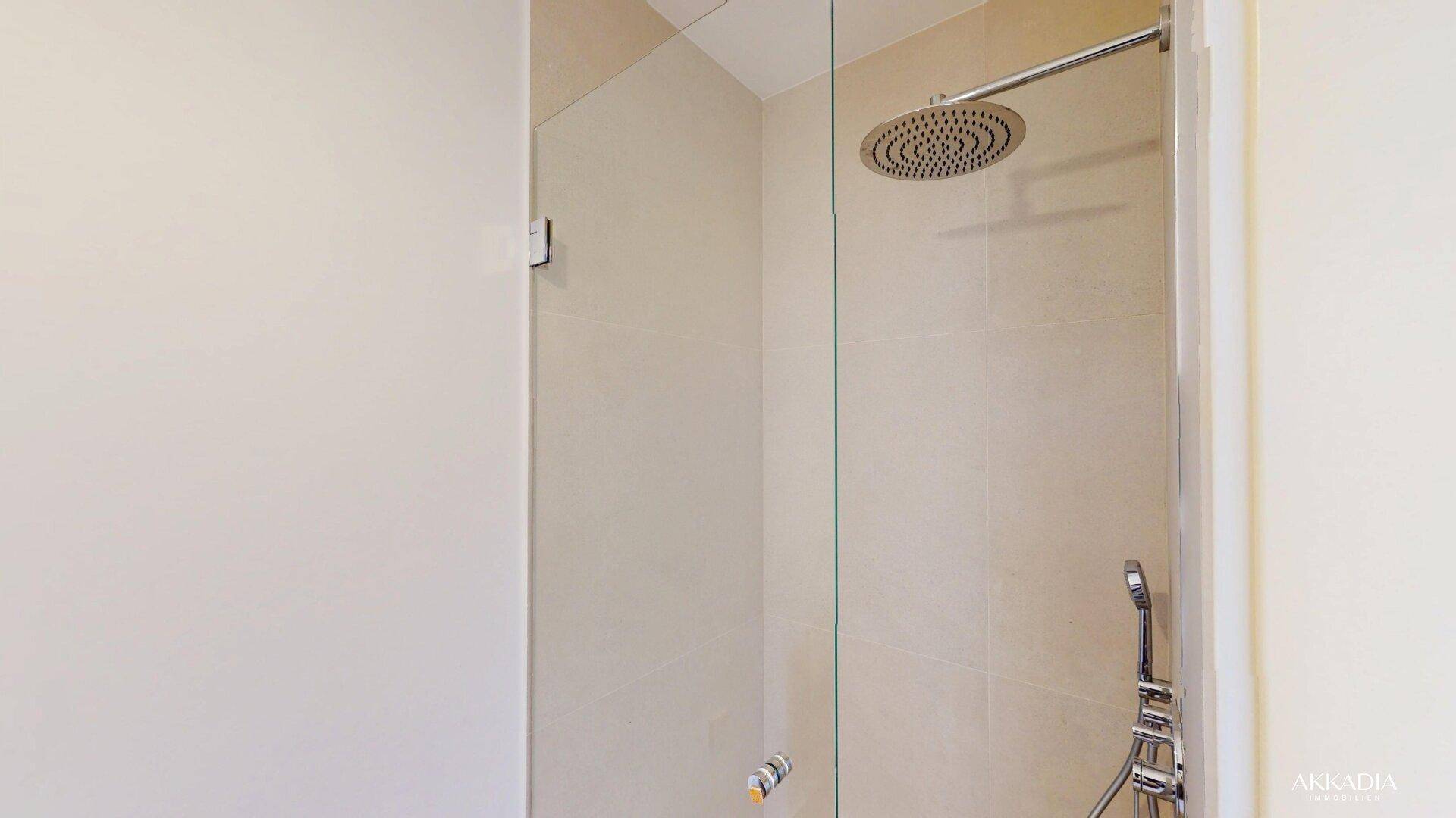 Moderne Dusche mit Regenduschkopf und Glasabtrennung in einem hellen Badezimmer.