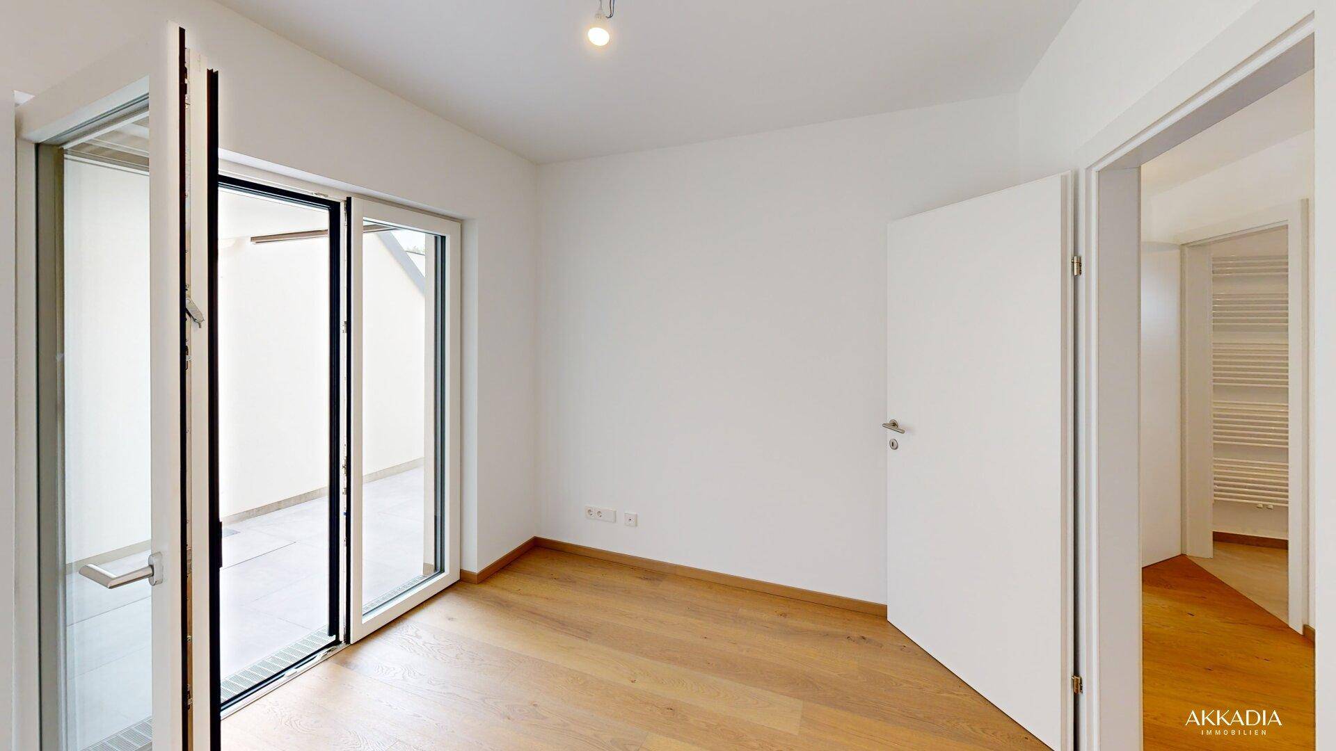 Helles Schlafzimmer mit Holzparkettboden und direktem Zugang zu einem Balkon oder einer Terrasse.