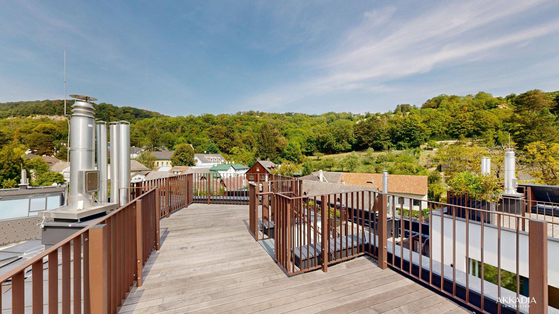 Weitläufige Dachterrasse mit Holzboden und Panoramablick auf die grüne Umgebung und die Stadt.
