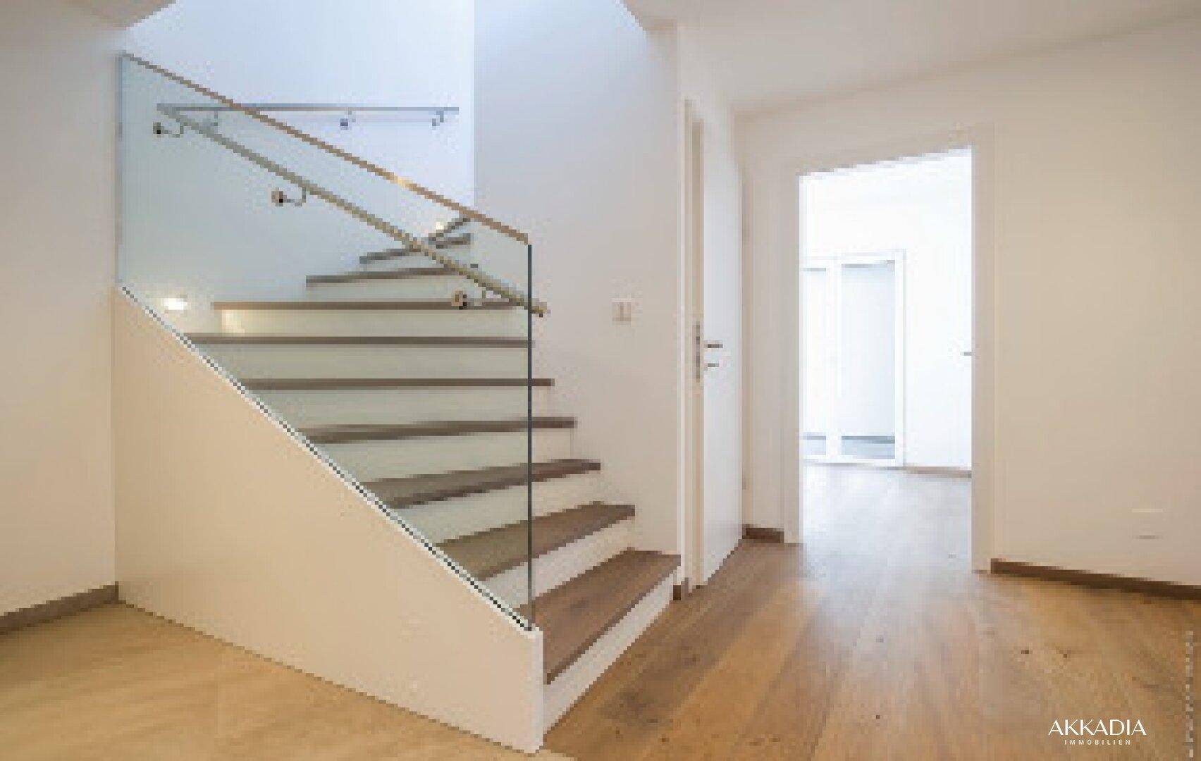 Heller Flur mit moderner Holztreppe, Glasgeländer und Zugang zu weiteren Räumen.