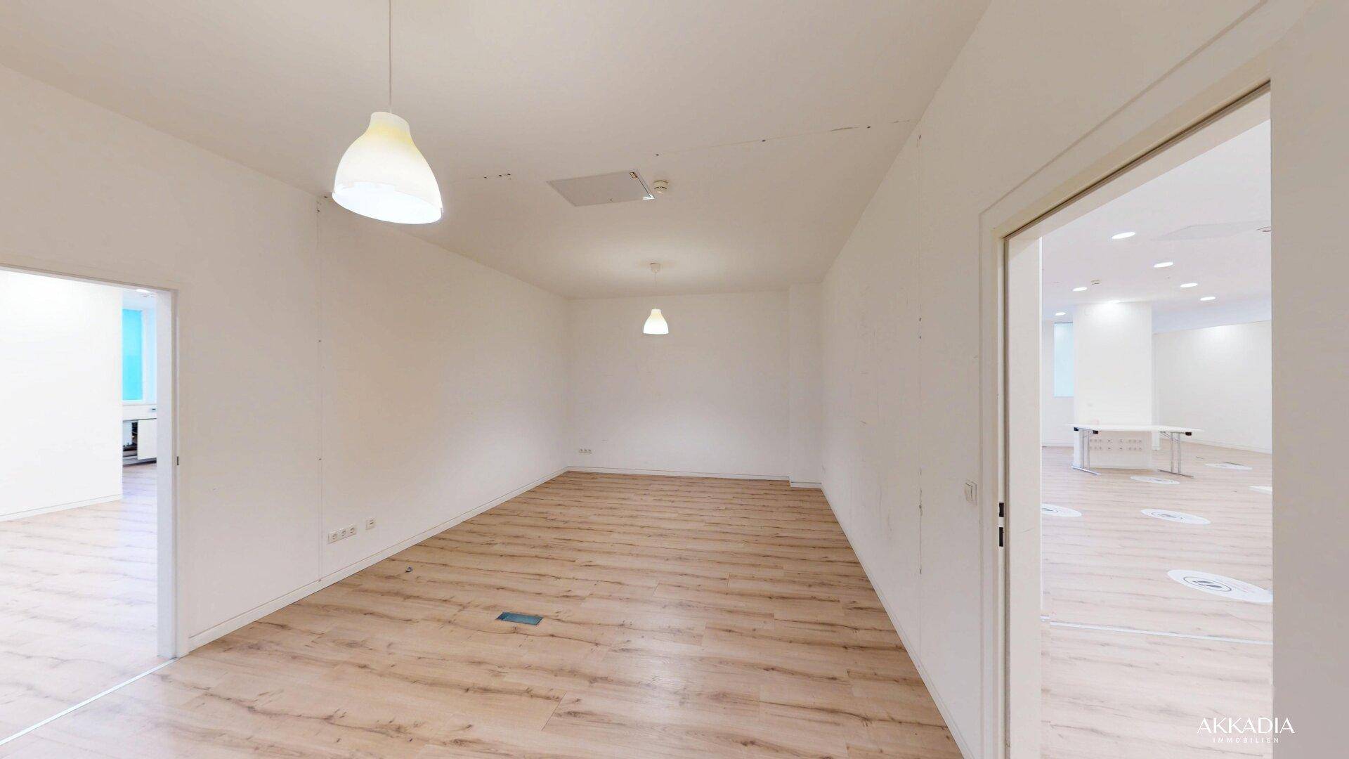 Leerer Büroraum mit Holzboden und Pendelleuchten, bietet eine flexible Arbeitsfläche.