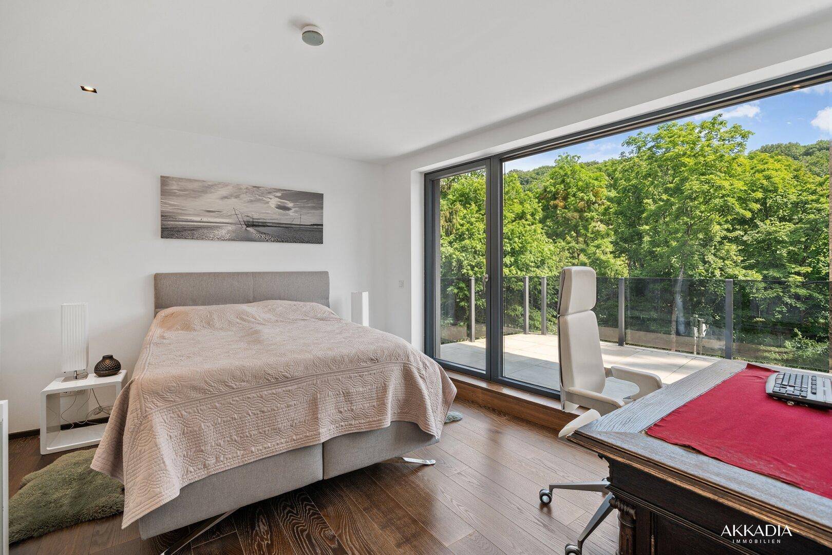 Helles Schlafzimmer mit Holzboden, raumhohen Fenstern und Zugang zu einem Balkon mit Grünblick.