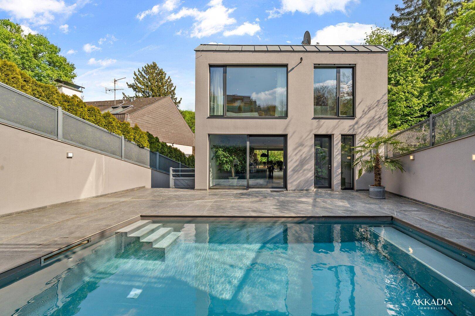 Moderne Villa mit Außenpool und großzügiger Terrasse, umgeben von viel Grün und Bäumen.