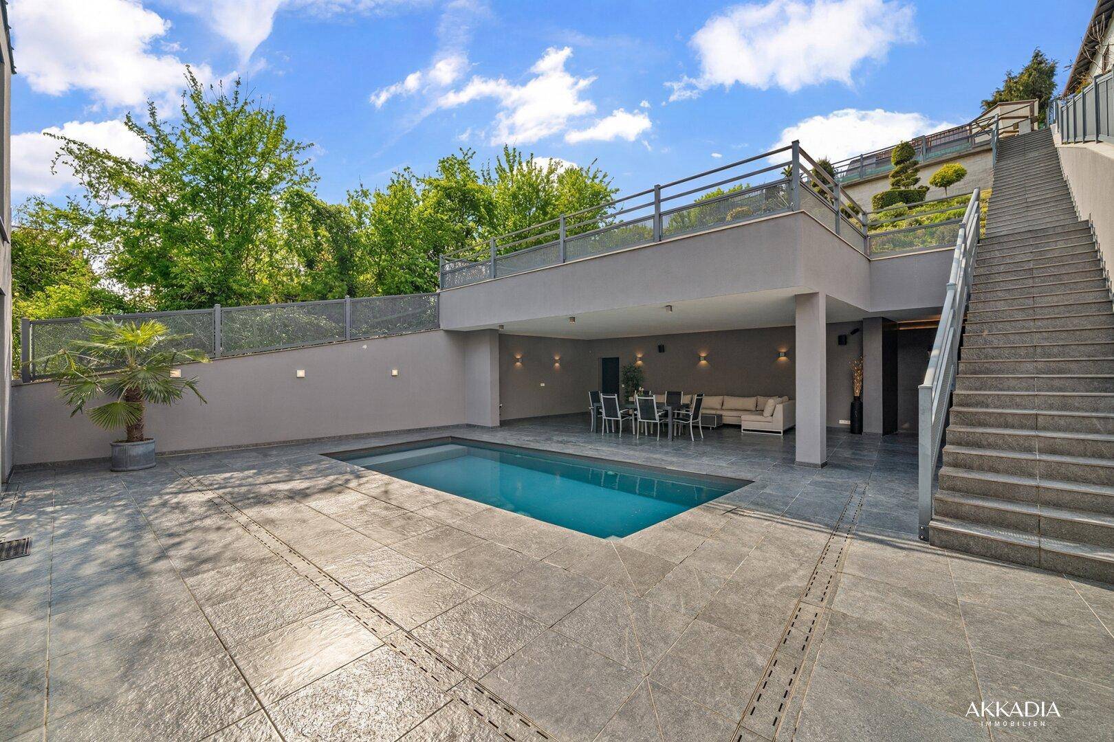 Außenbereich mit Pool, überdachtem Sitzbereich und Treppe zum oberen Gartenbereich.