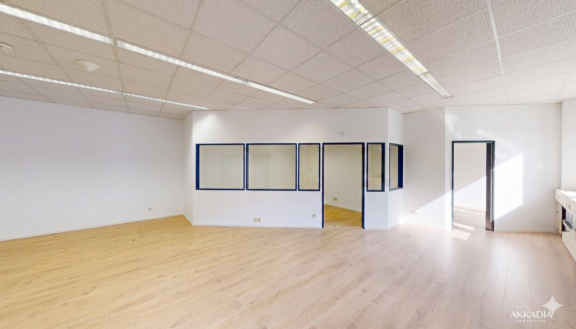Großzügiger Bürobereich mit Trennwänden und Fenstern, die Tageslicht hereinlassen, sowie einem hellen Laminatboden.