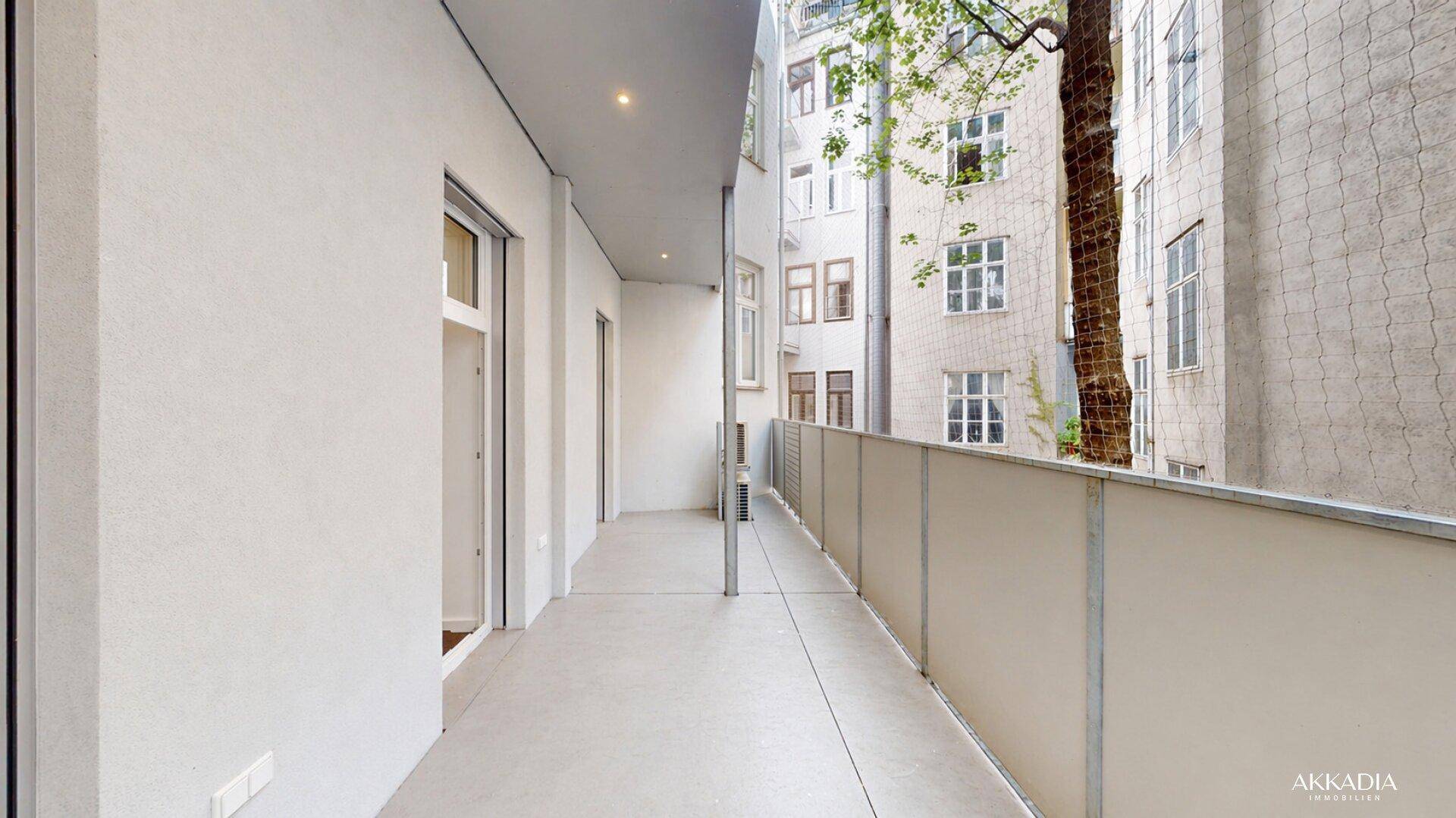 Langer, schmaler Balkon mit Blick auf den Innenhof und angrenzende Gebäude.
