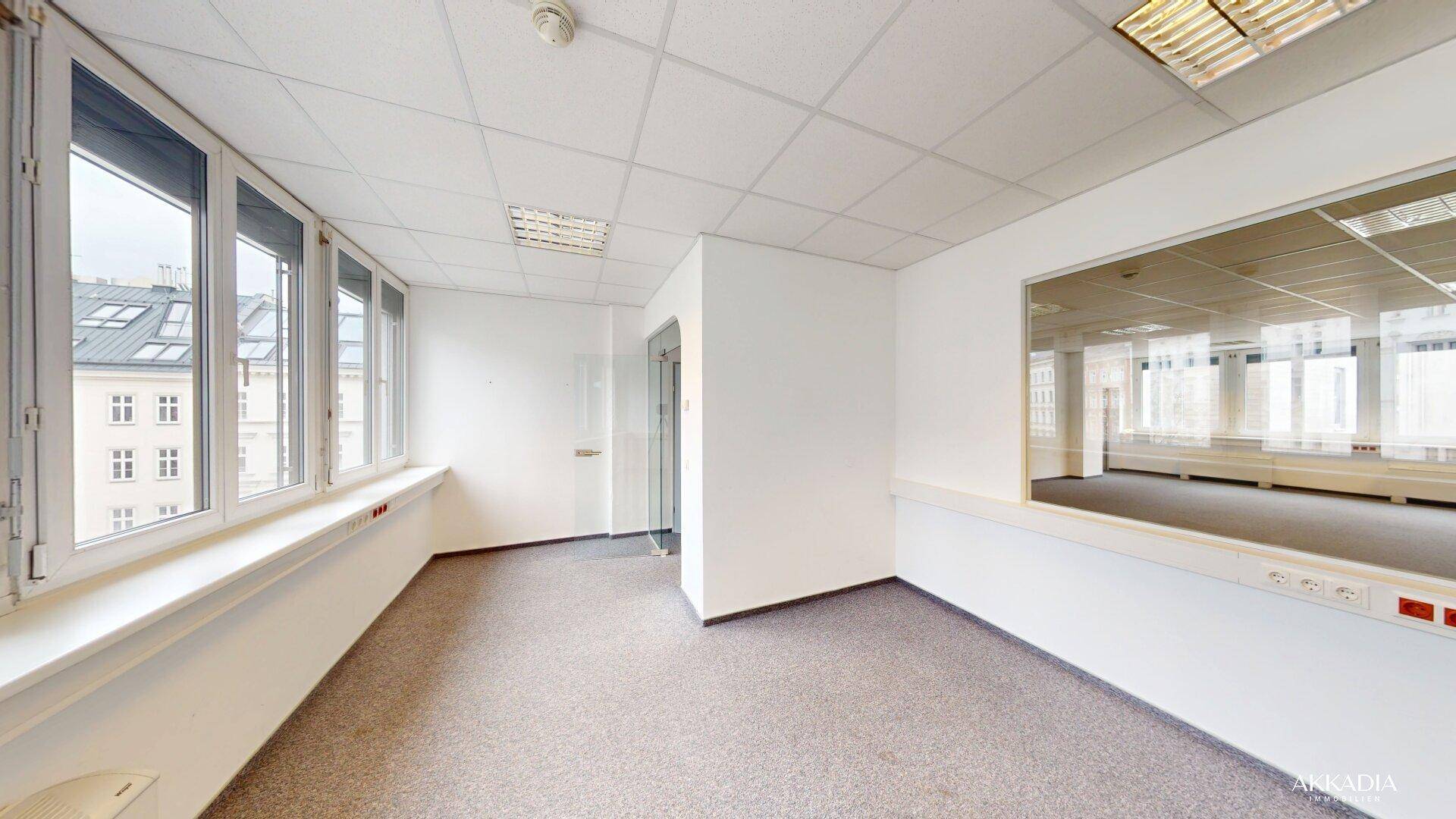 Helles Büro mit Teppichboden, großen Fenstern und Blick auf die Stadt, ausgestattet mit Rasterdecken.